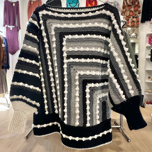 Black, gray, and white striped sweater with pom-poms on a rack in a store setting