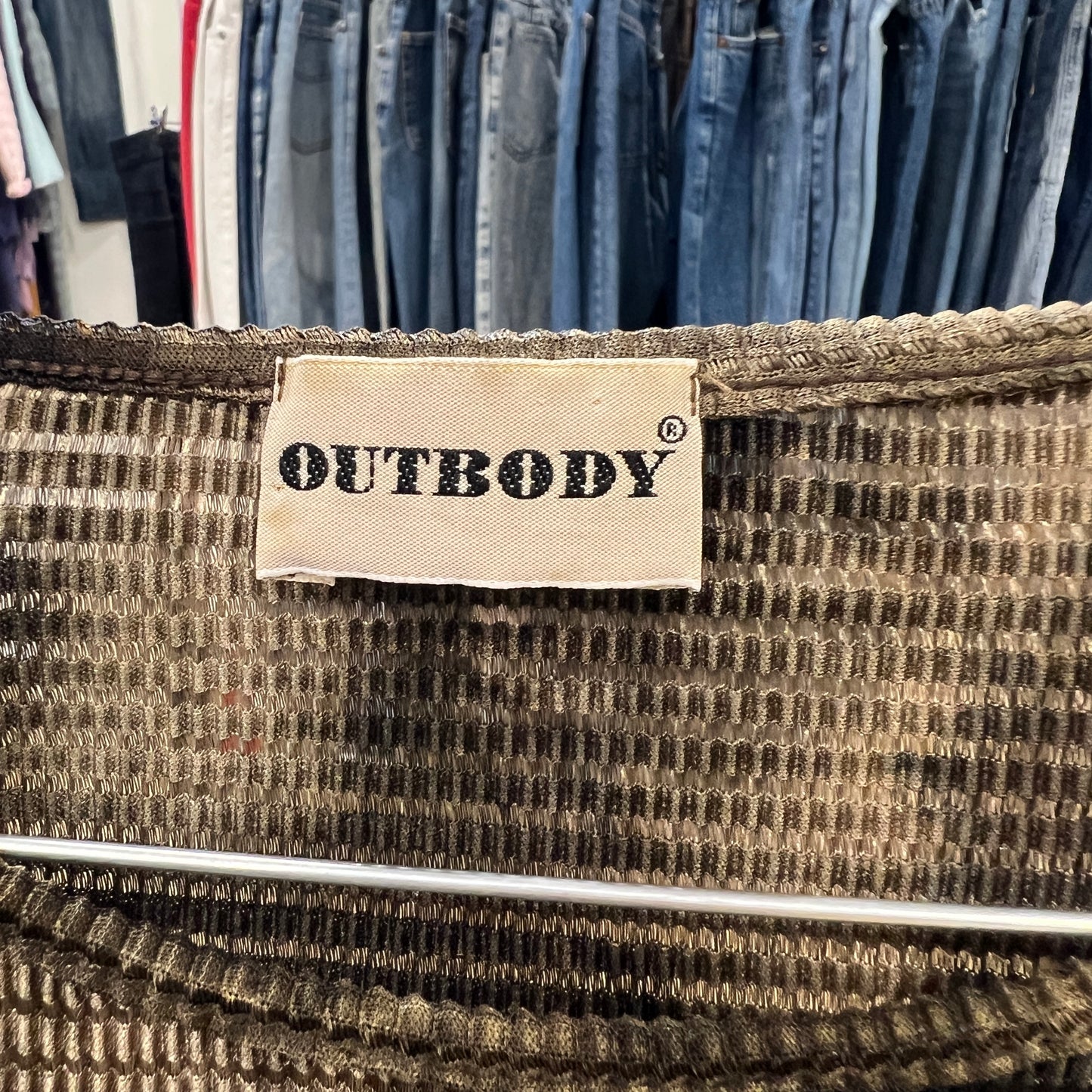 Textile product with 'OUTBODY' label against a background of hanging clothes