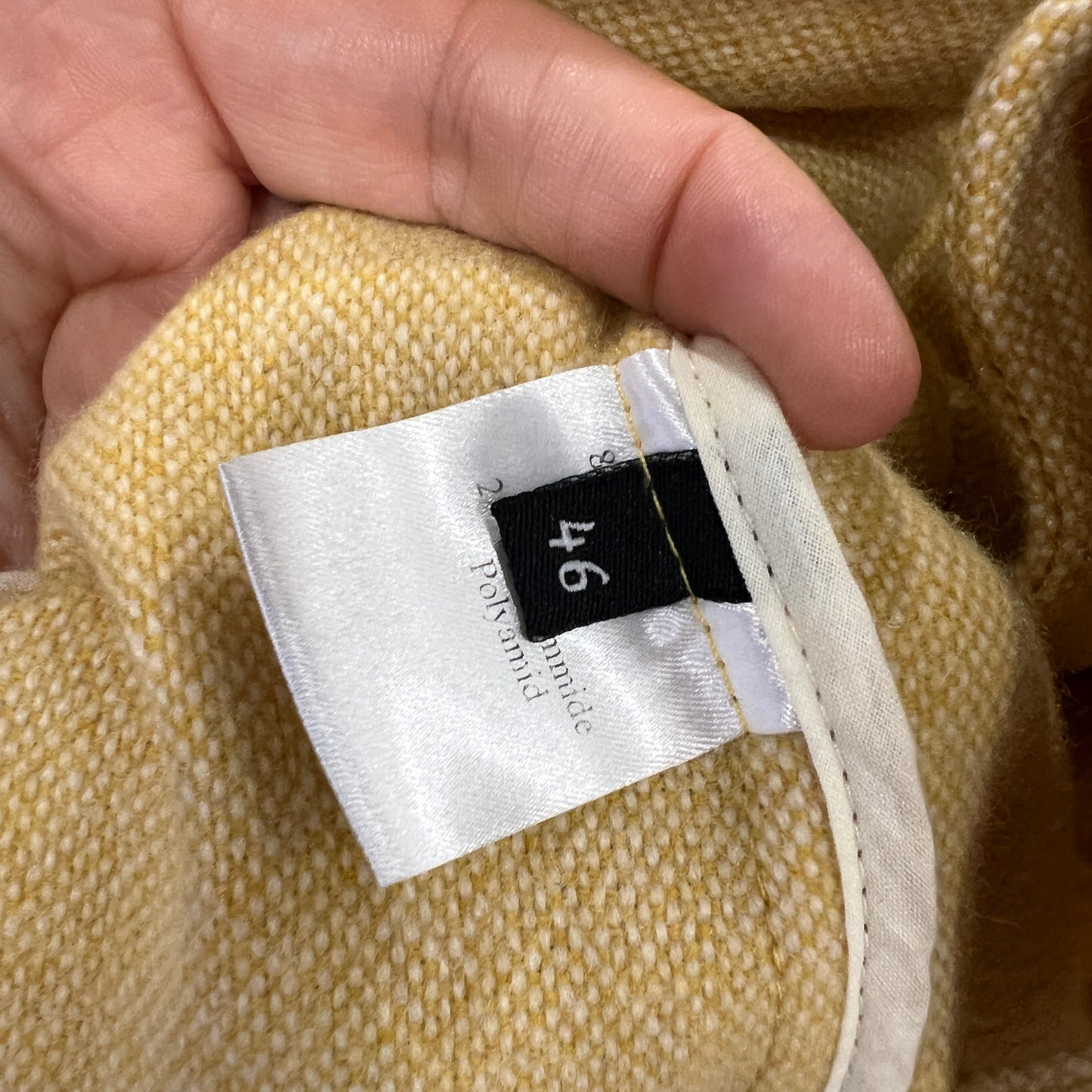 Close-up of a beige fabric with a size tag labeled '46' held by a hand