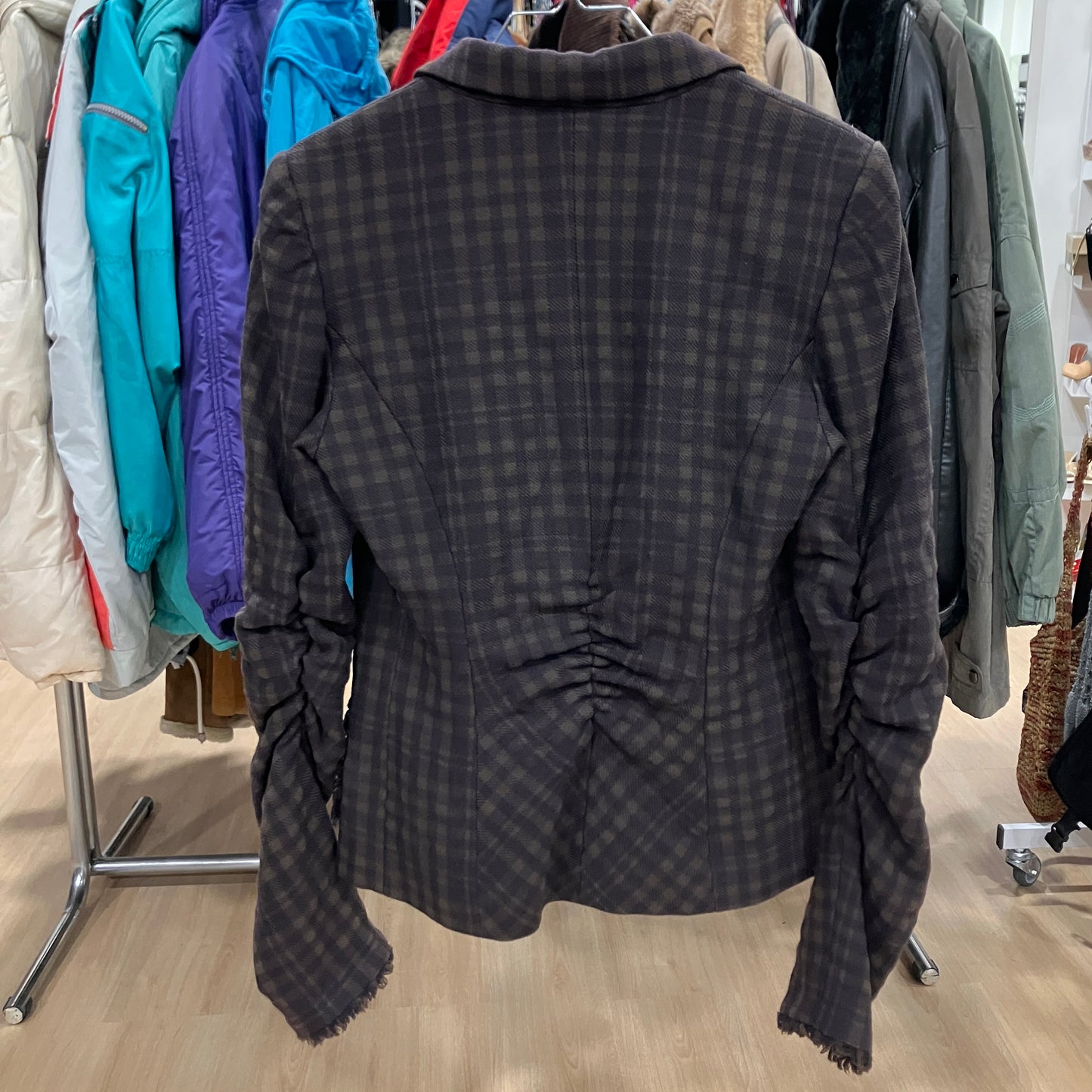 Dark plaid jacket on a hanger with a clothing rack in the background