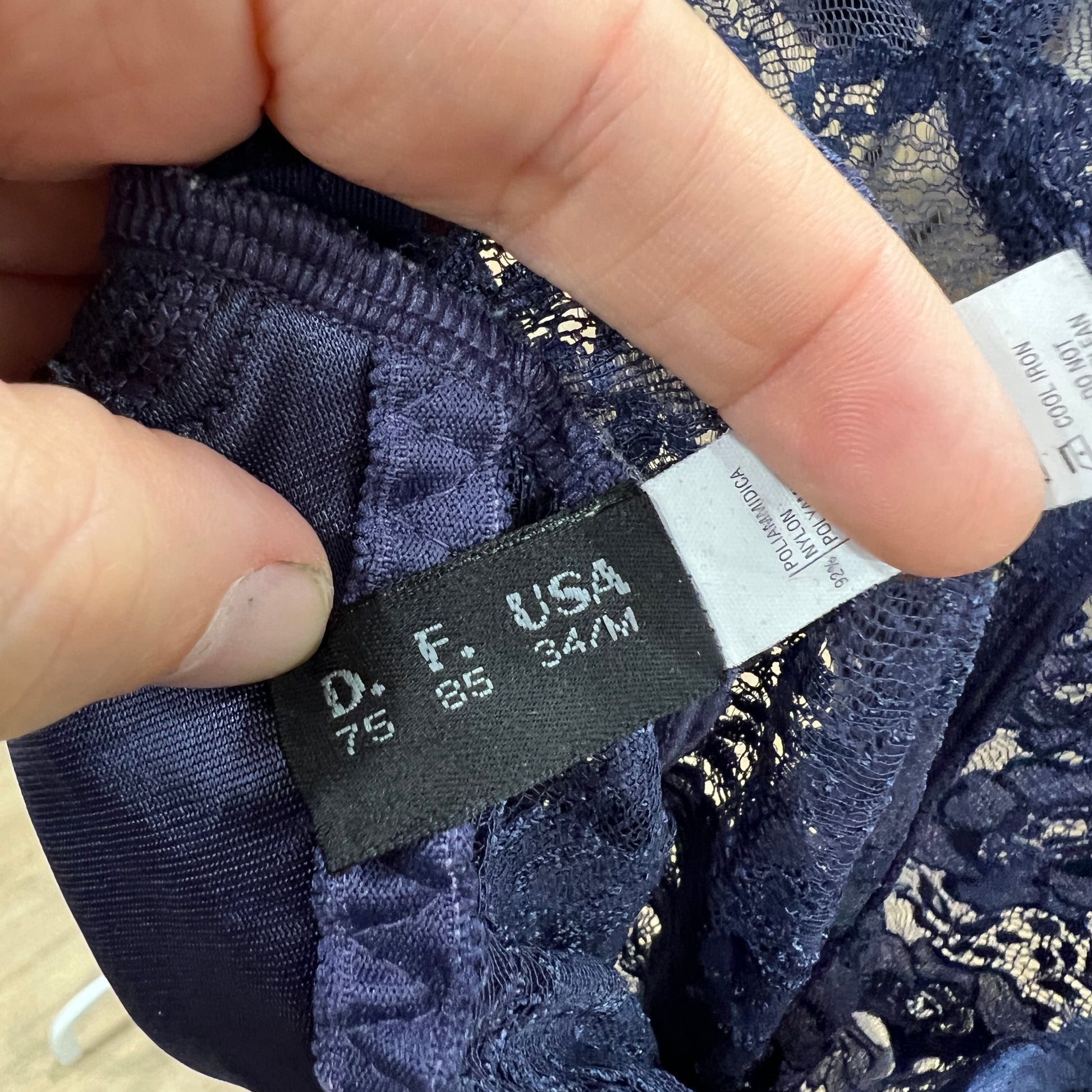Navy lace garment with a label held by fingers