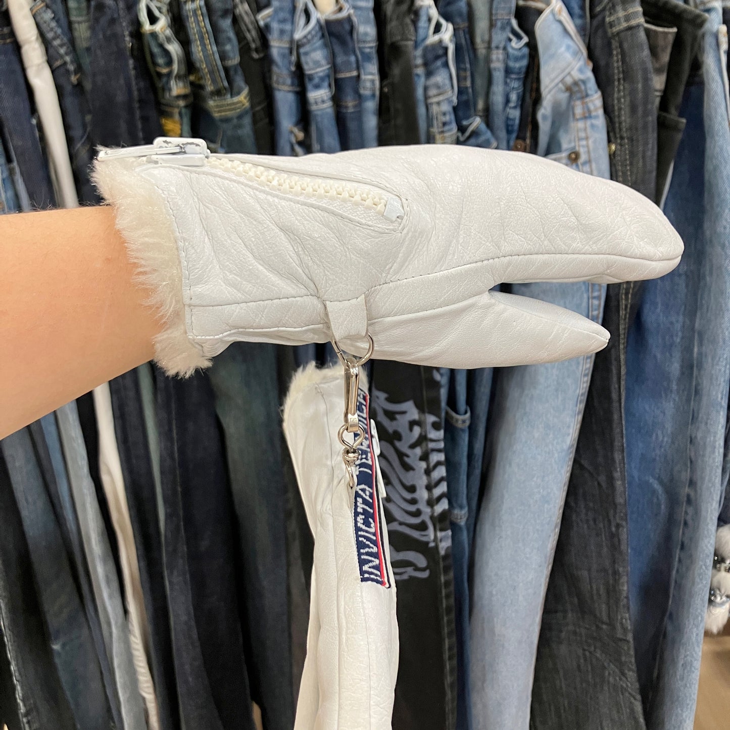 Light gray quilted jacket with fur trim held against a background of jeans on a rack