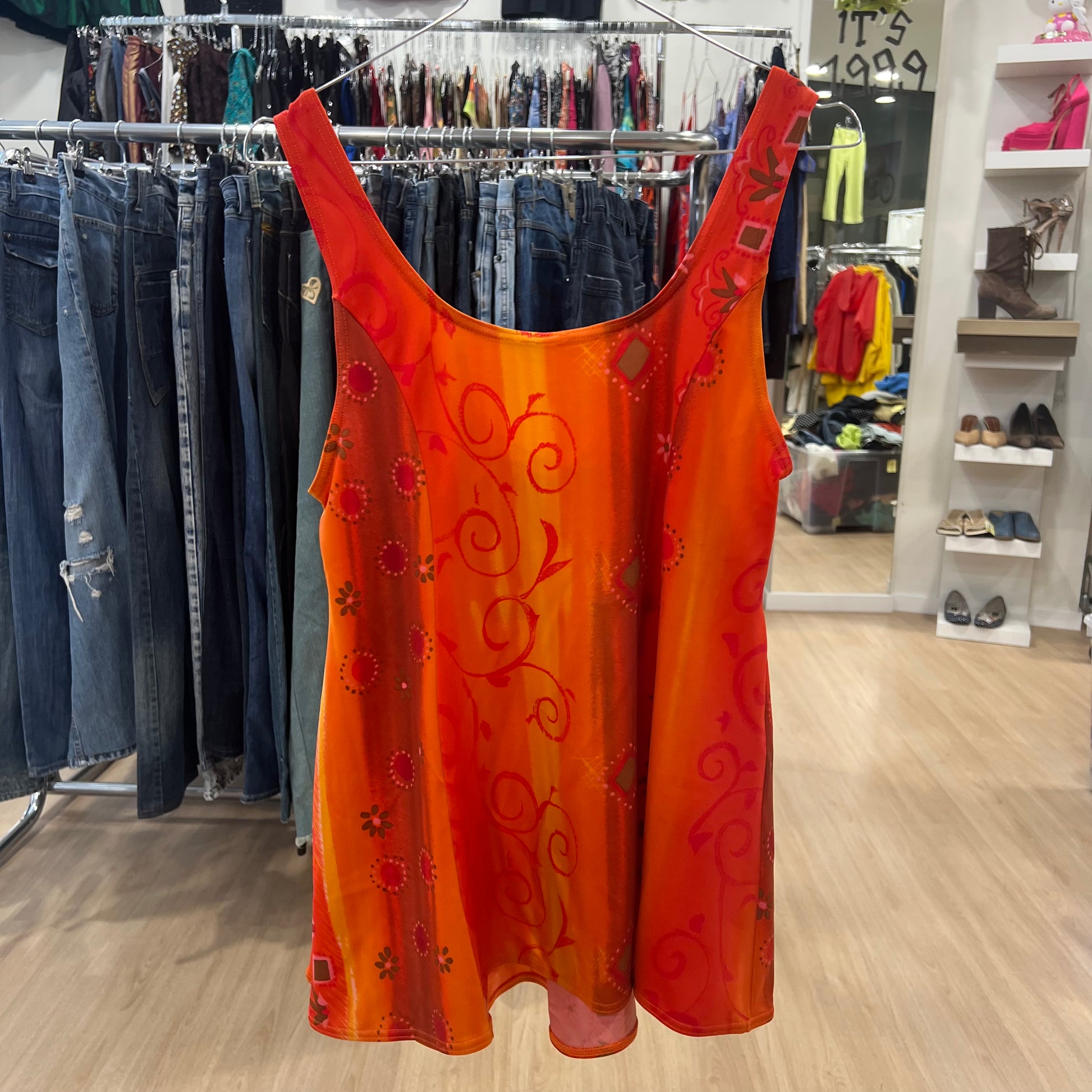 Orange sleeveless top with floral patterns hanging in a store setting