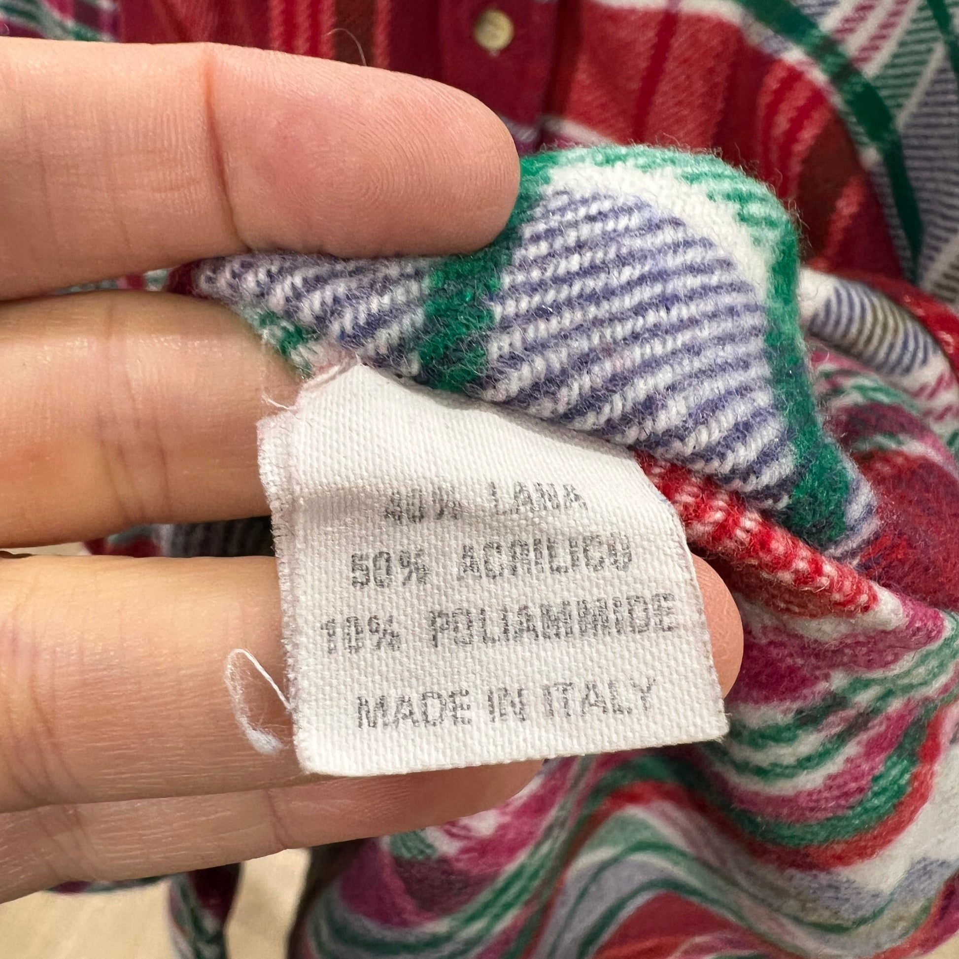 Fabric tag with material composition details held by a hand against a colorful fabric background