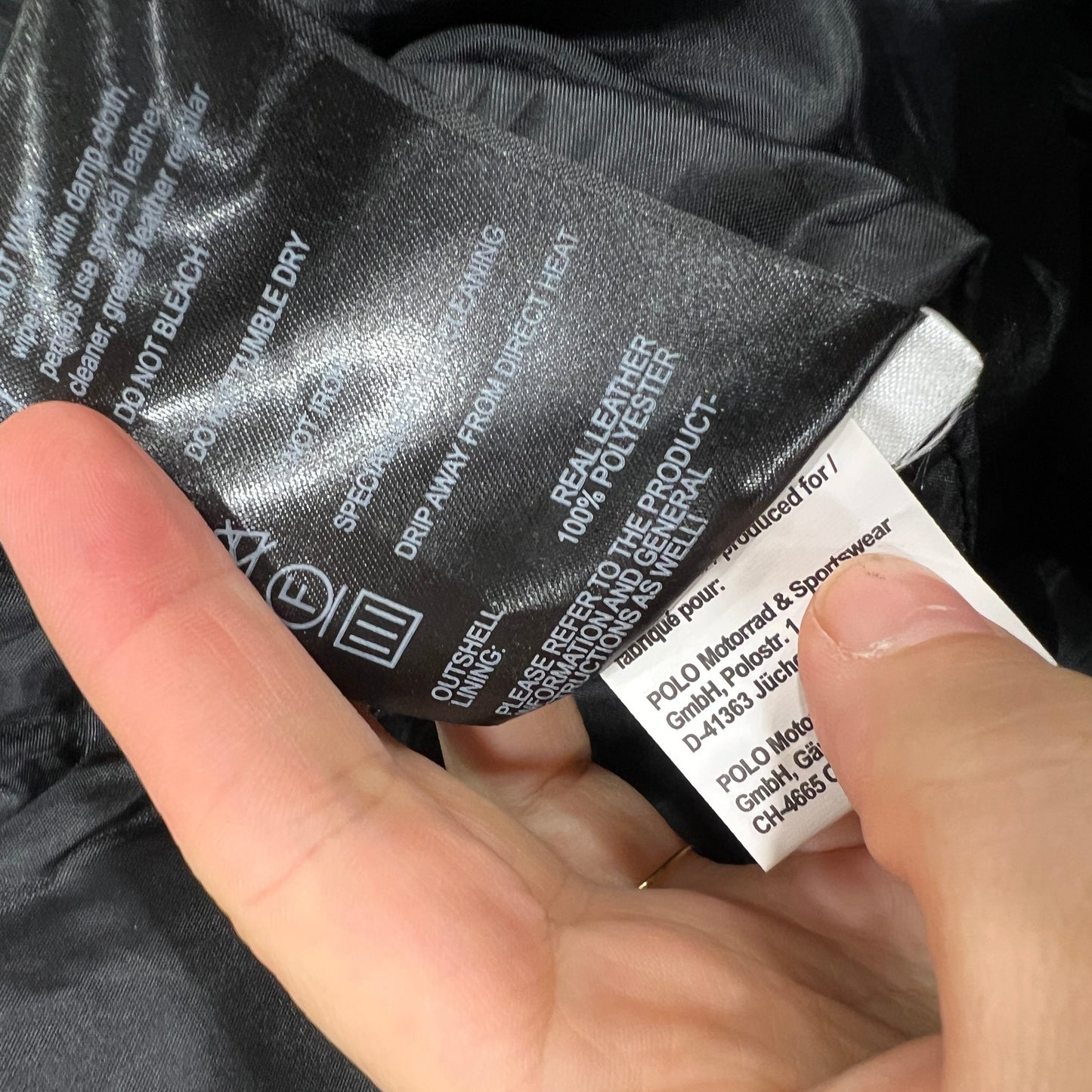Hand holding a clothing label with text on a black garment