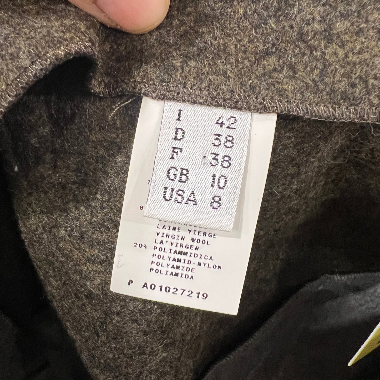 Close-up of a size and composition label inside a Pollini wool skirt, showing Italian size 42 with international equivalents and a fabric mix of virgin wool and polyamide, held between two fingers
