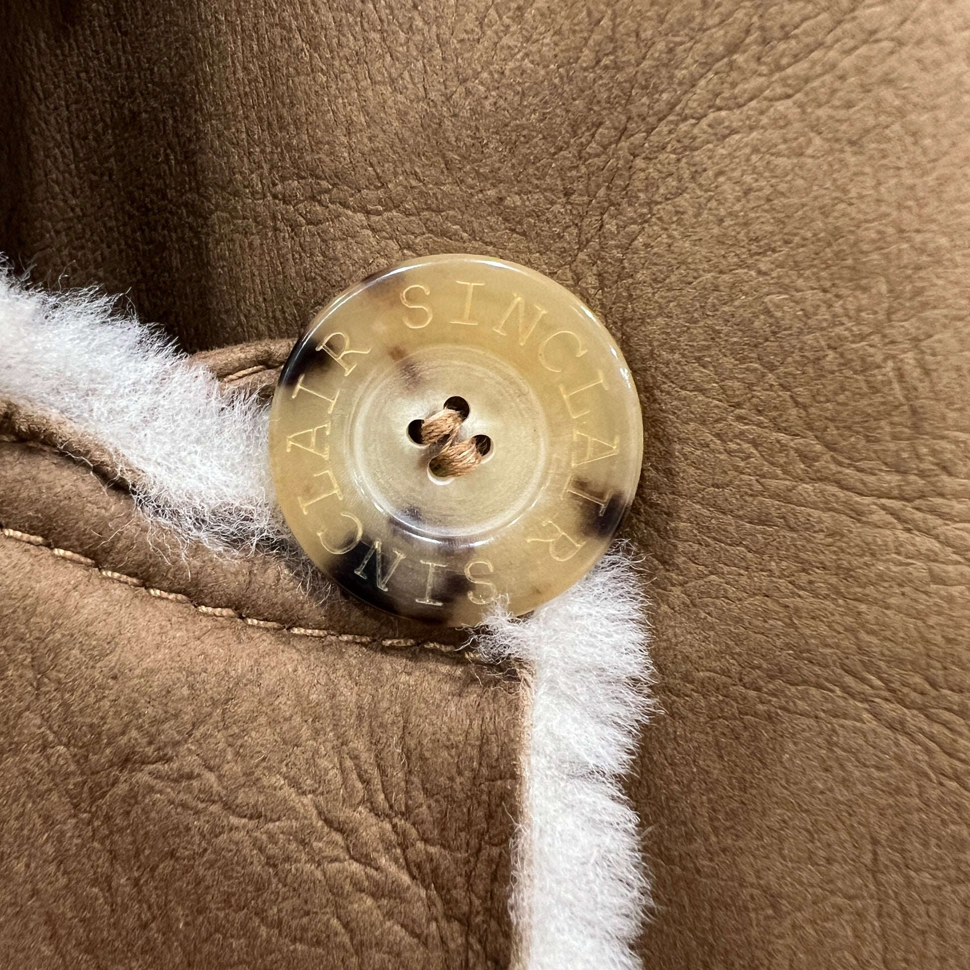 Close-up of a gold button with 'SINCLAIR' engraving on a brown leather surface