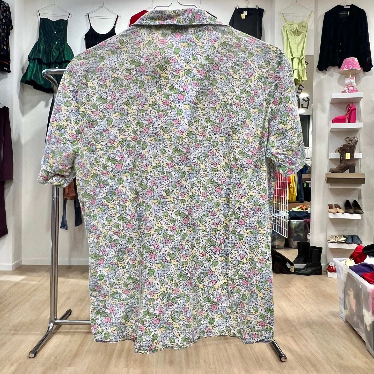 Floral patterned shirt on a hanger in a store setting with clothing racks and shelves in the background