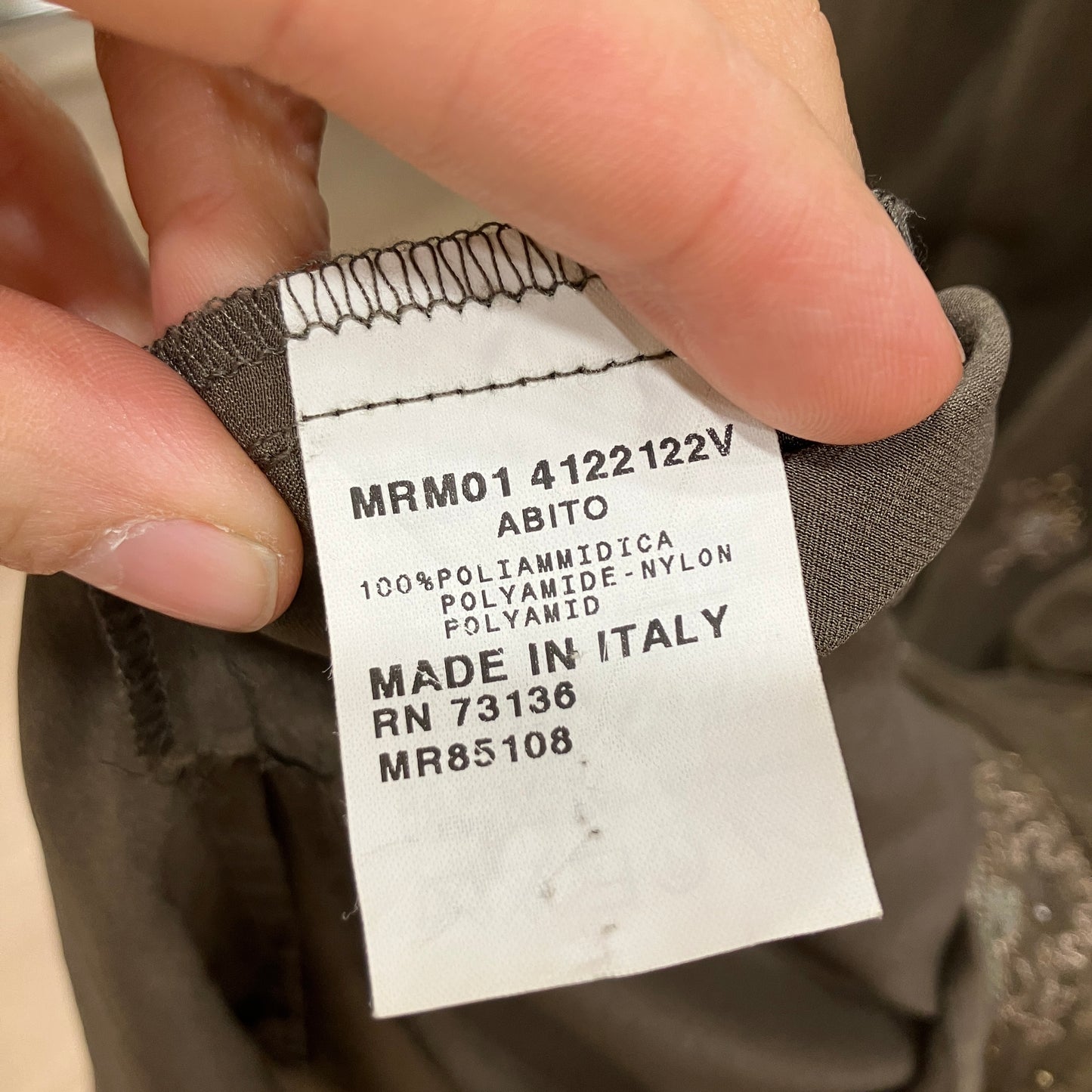 Clothing label with text on a garment, held by a hand
