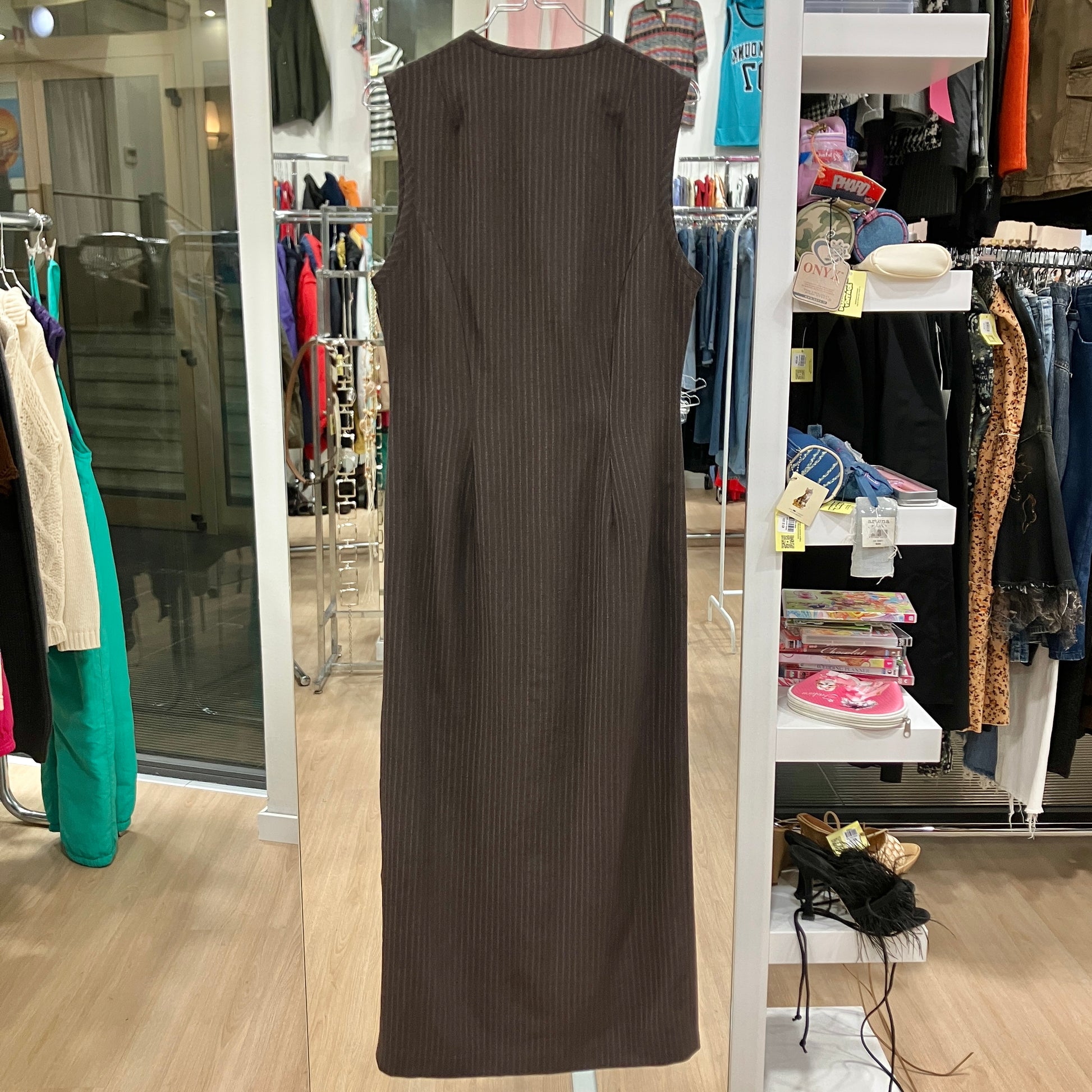 Brown sleeveless dress hanging in a store with various clothing items in the background
