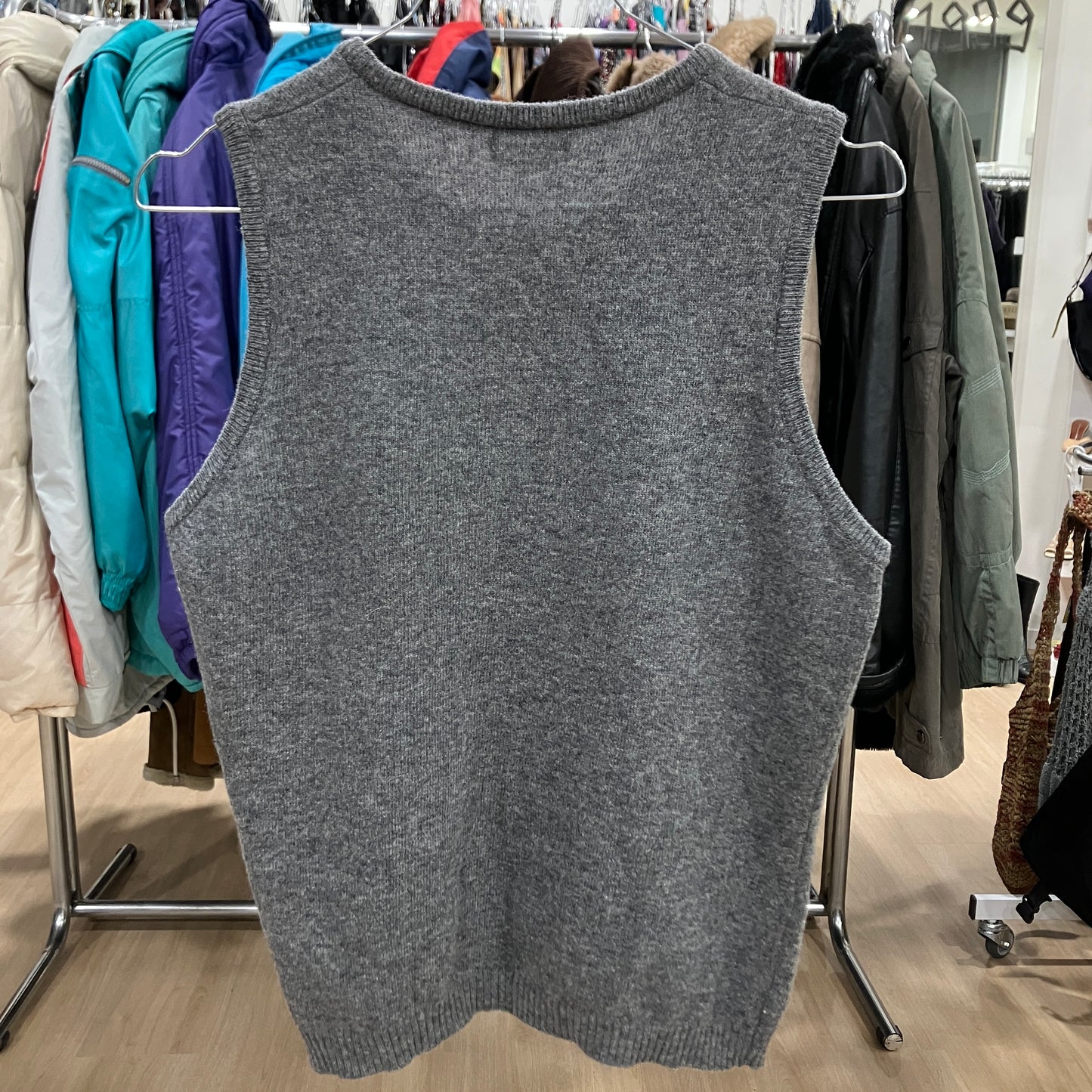 Gray sweater vest hanging on a rack with other clothing in a store setting