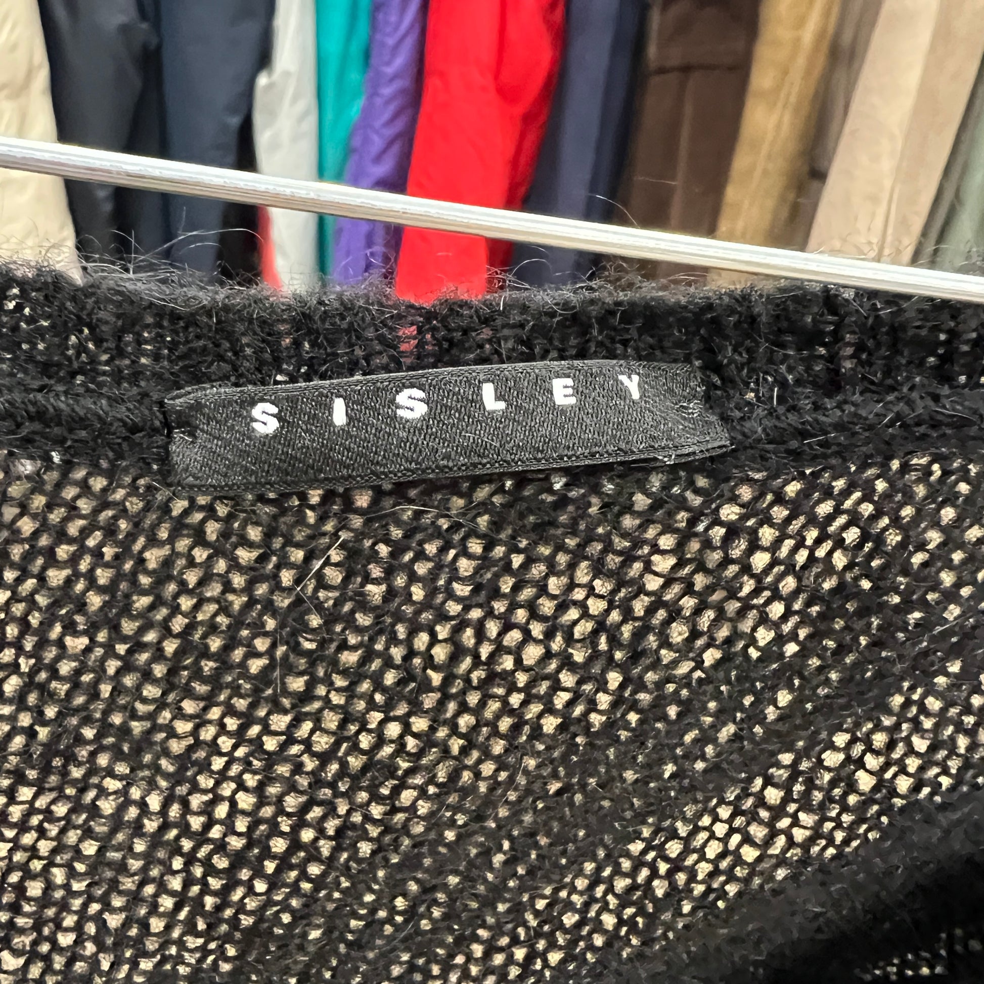 Black textured fabric with 'Sisley' label against a blurred clothing background