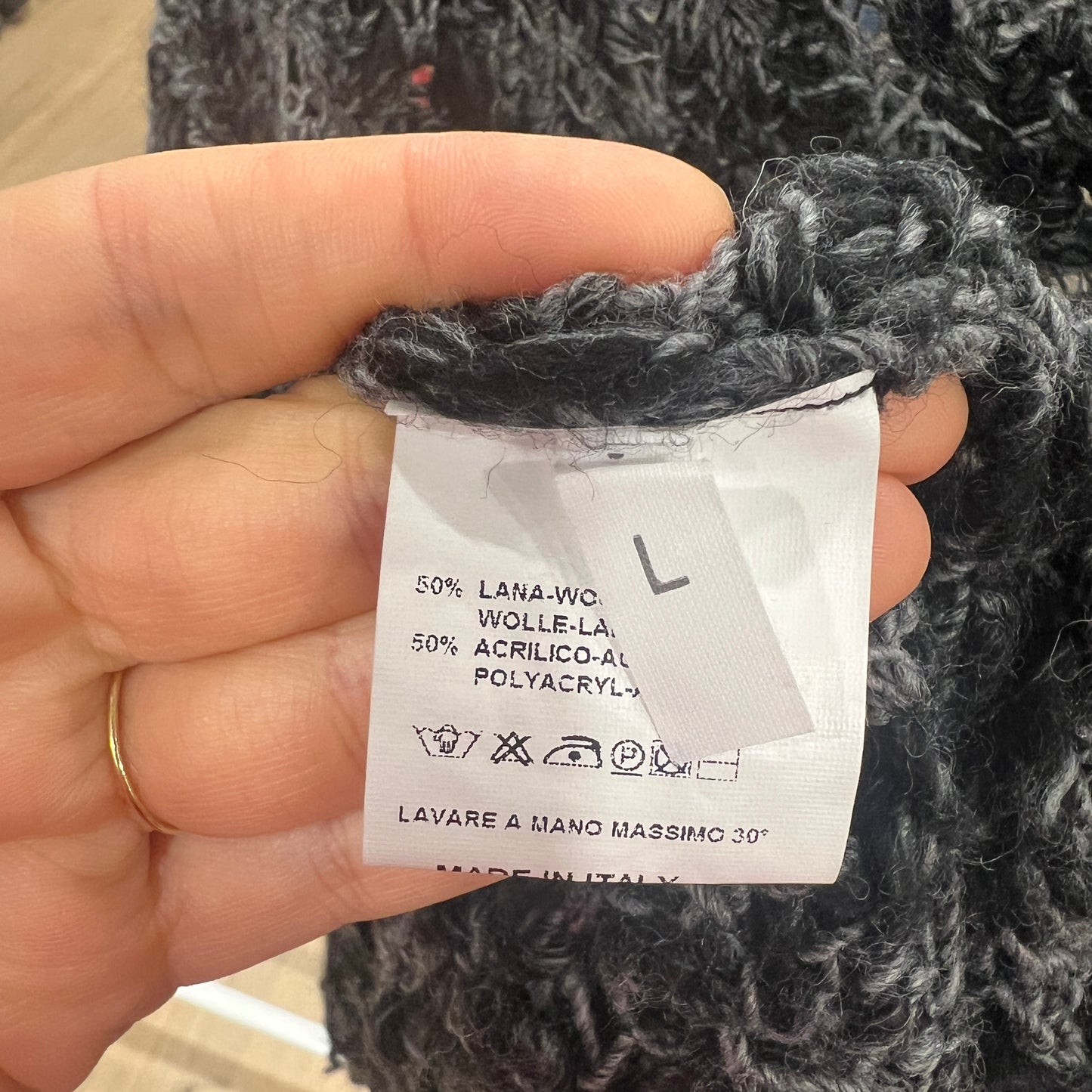 Hand holding a label on a knitted garment with text and symbols