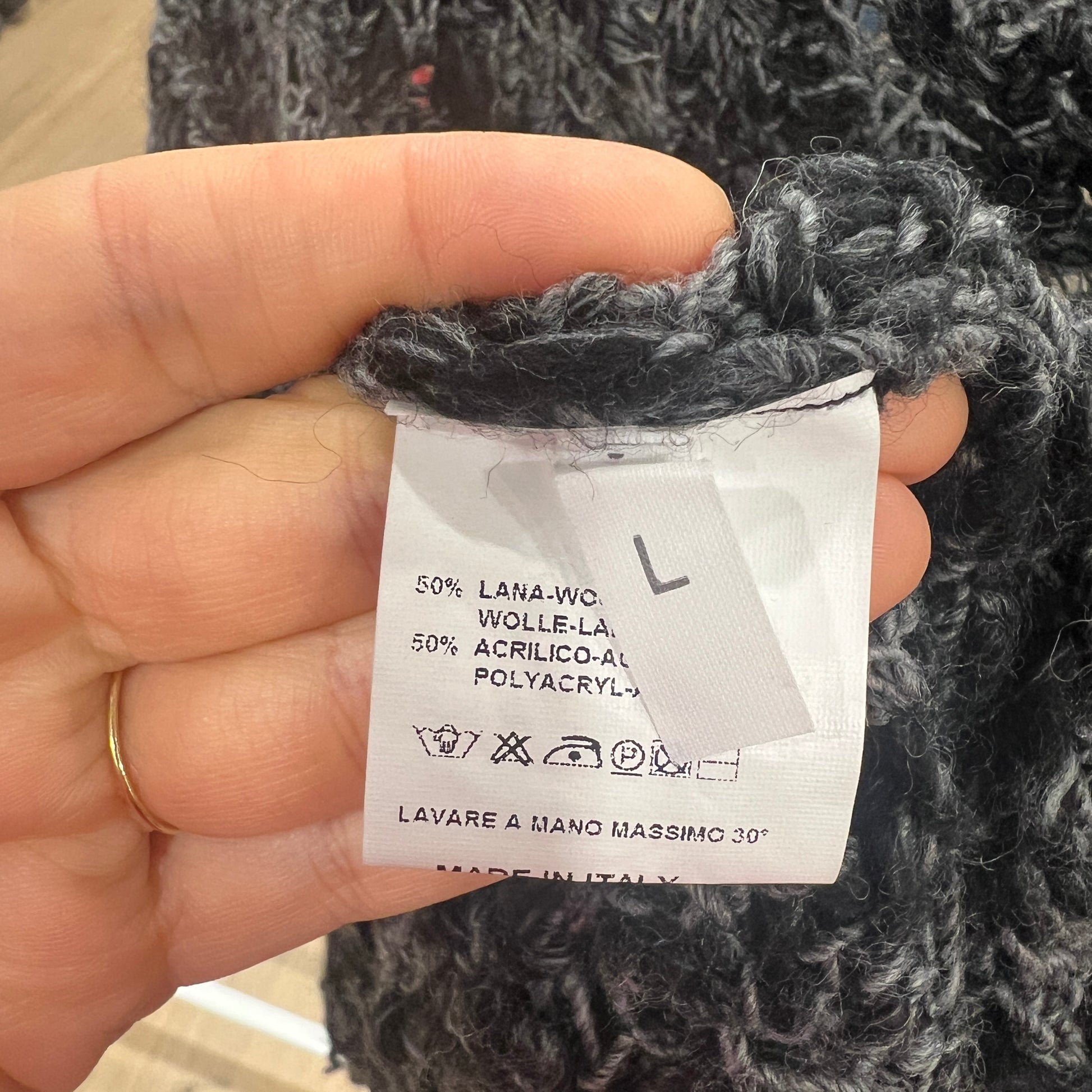 Hand holding a label on a knitted garment with text and symbols
