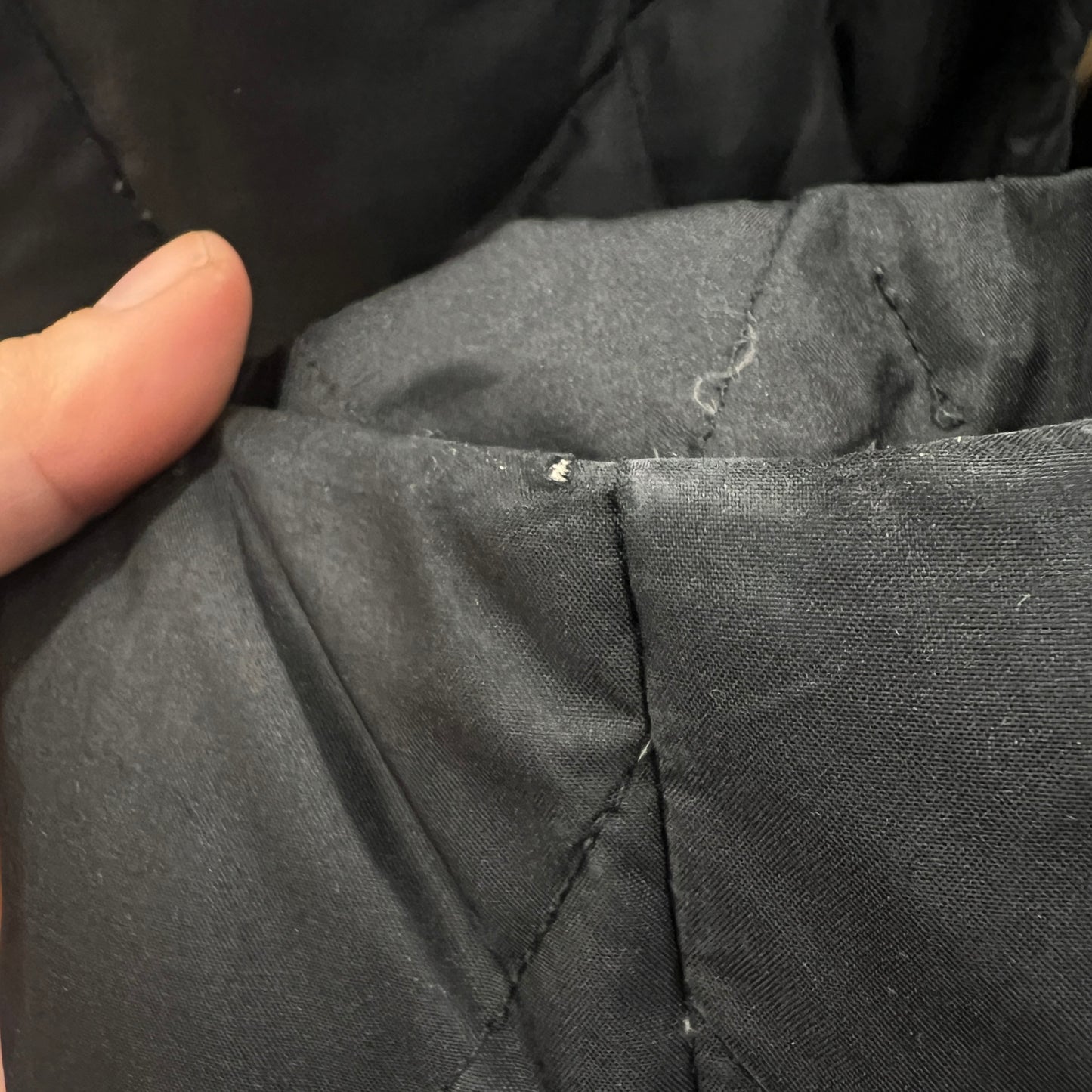 Close-up of a person holding dark fabric with visible stitching