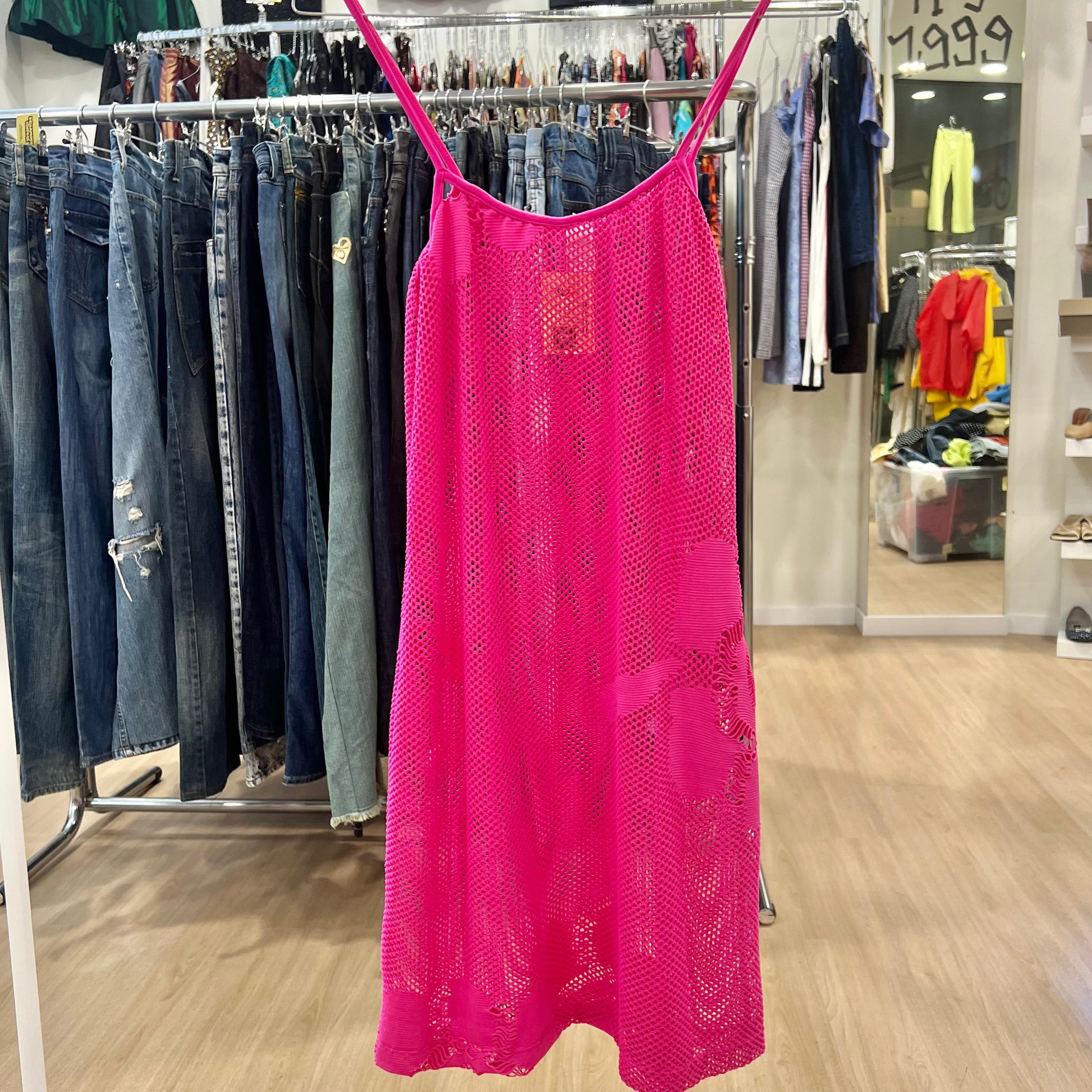 Pink lace dress hanging on a rack in a store with jeans and other clothing in the background