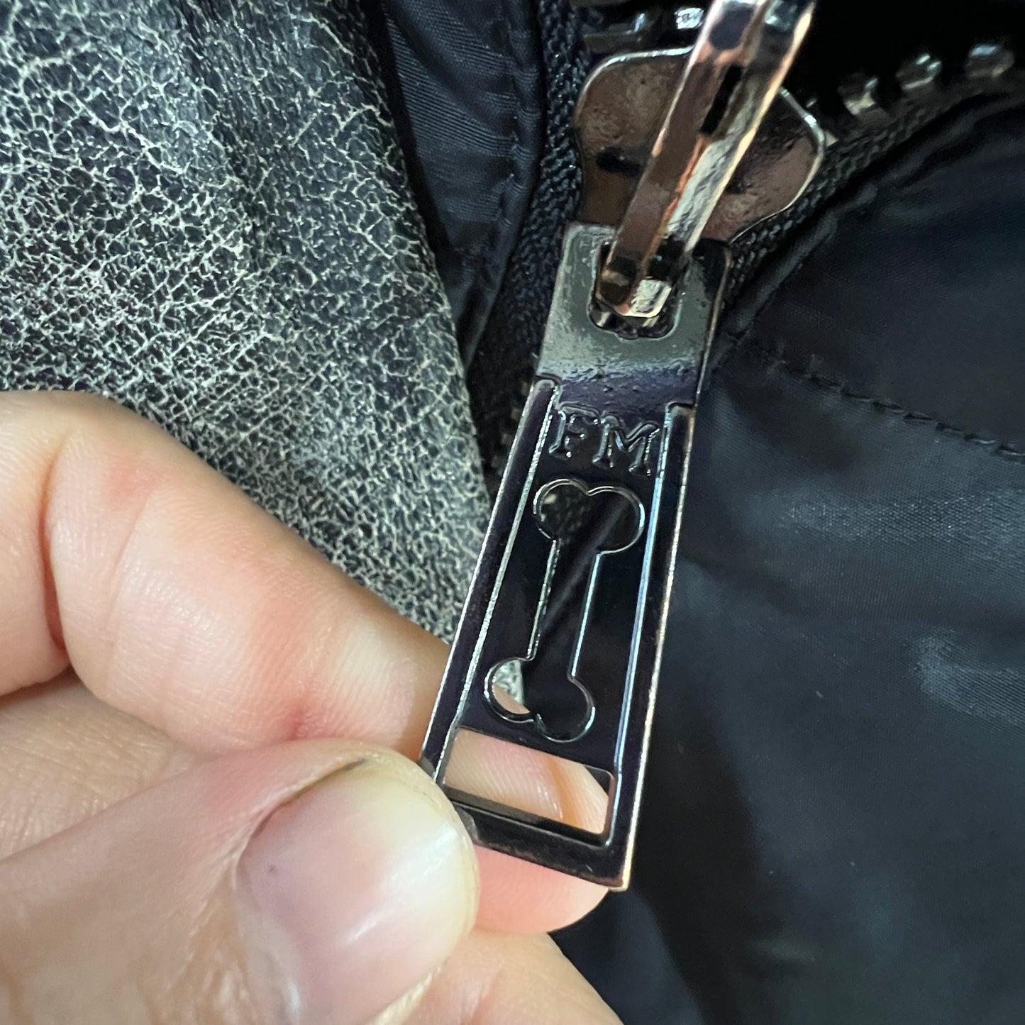 Close-up of a zipper pull being held by a hand, with a textured fabric background
