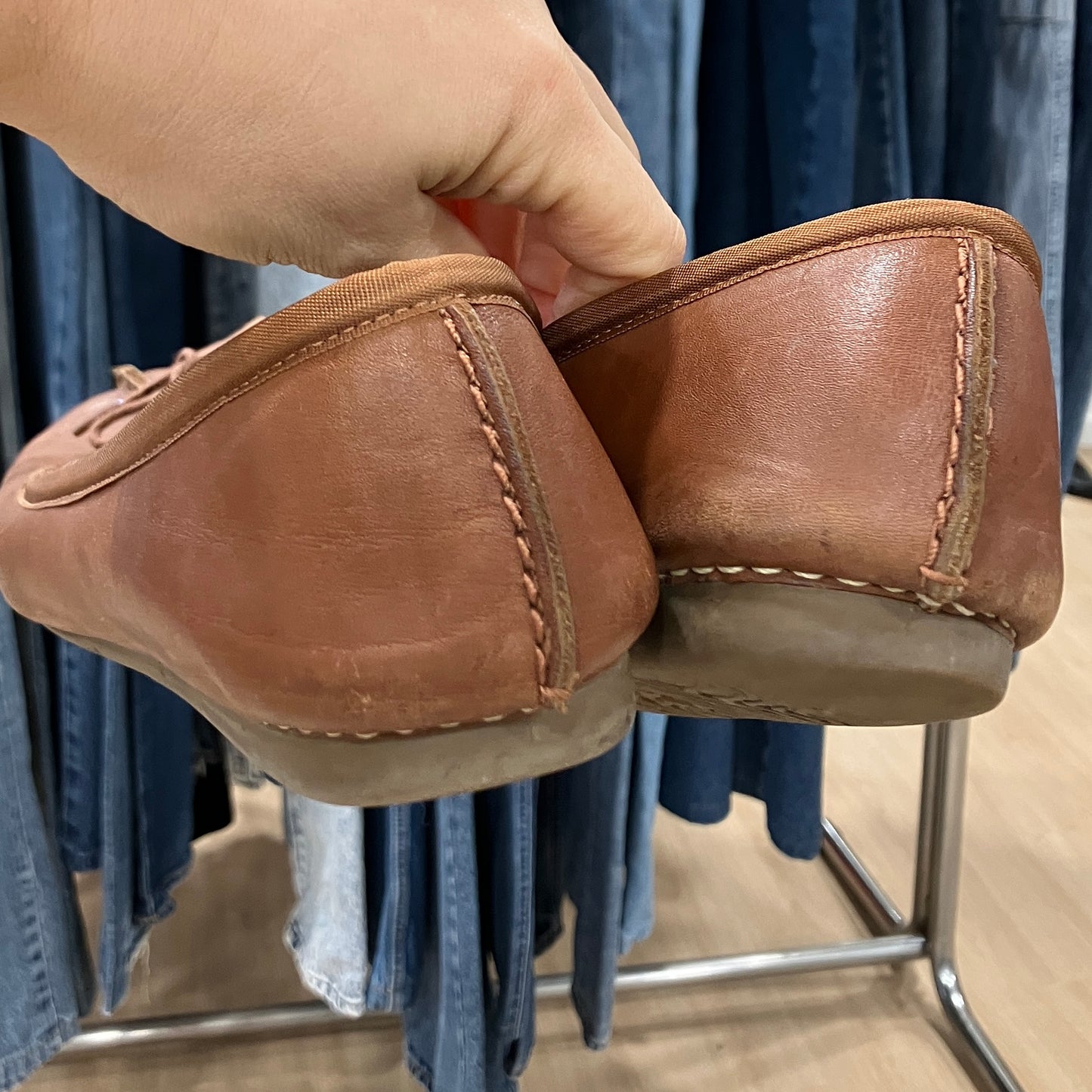 Brown leather shoes  held by a hand with a clothing store background