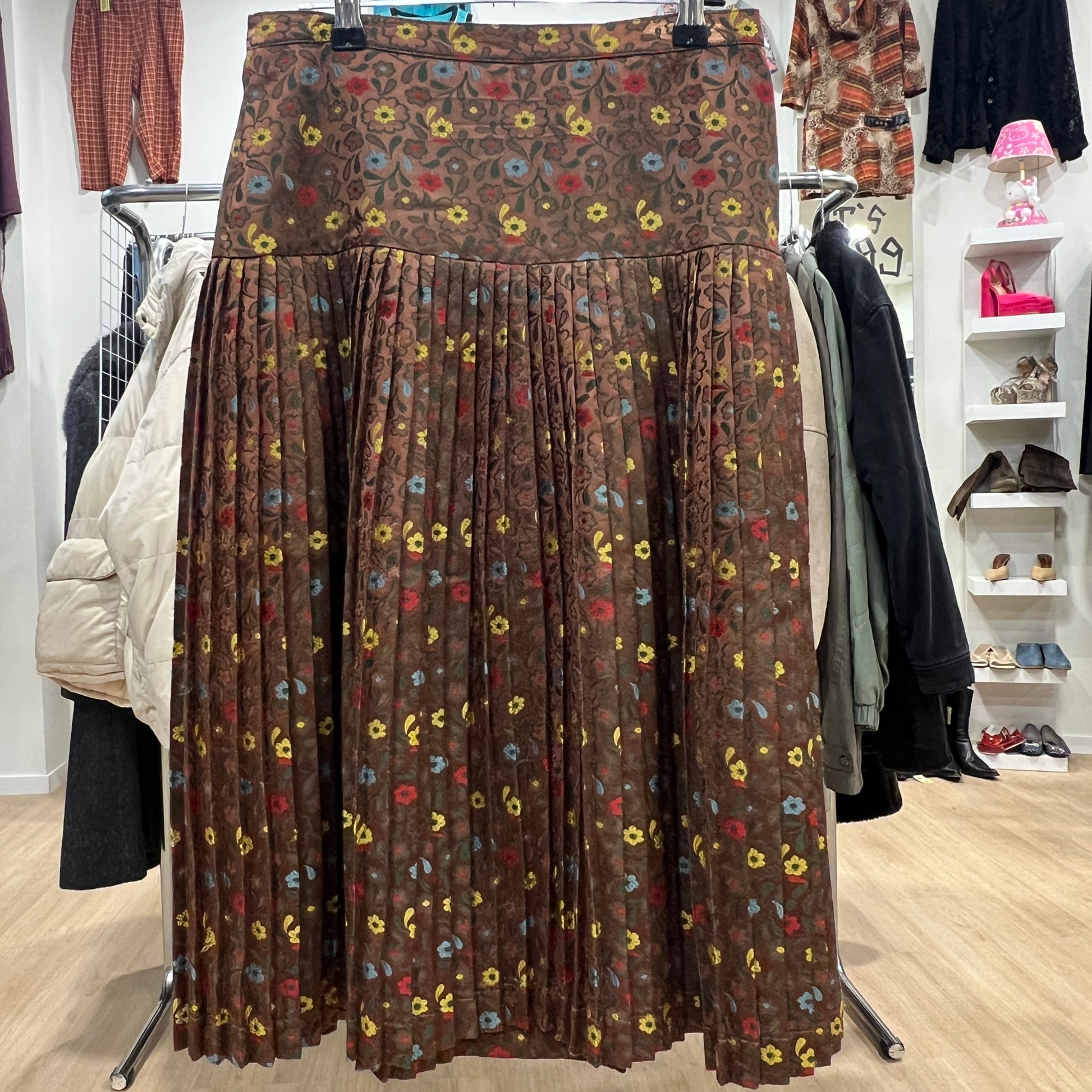 Brown floral-patterned skirt displayed in a store setting with clothing racks and shelves in the background