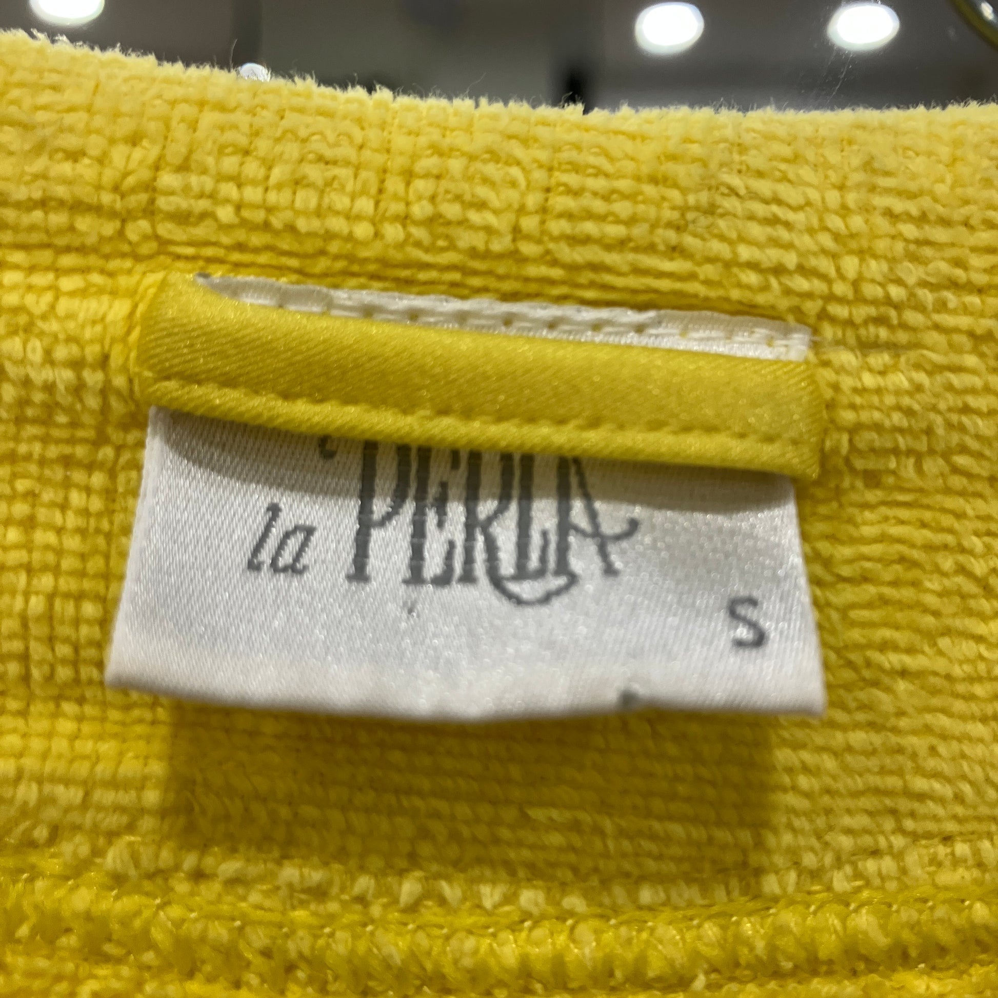 Yellow fabric with a 'la PERLA' label on a blurred background