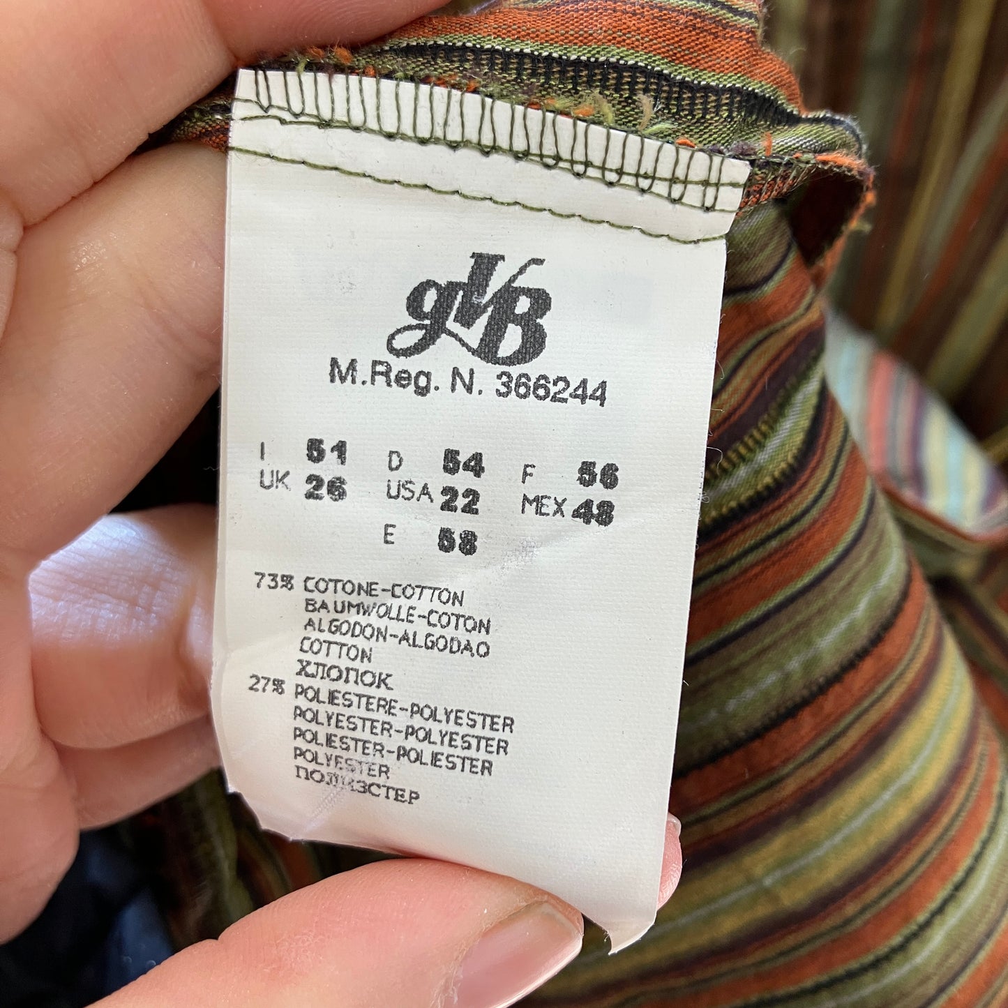 Clothing label with brand logo and size information held by a hand, with a striped garment in the background