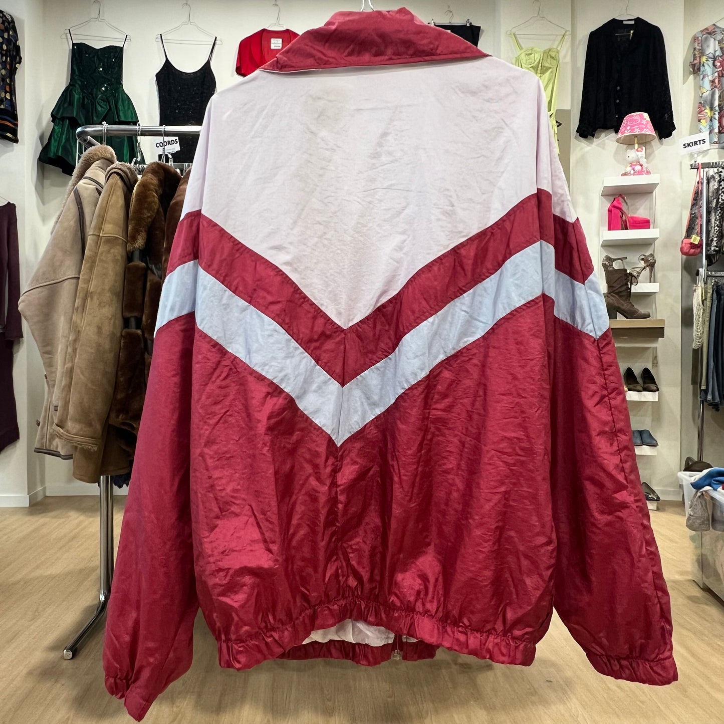 Red and white track jacket displayed in a store with clothing racks and shelves in the background