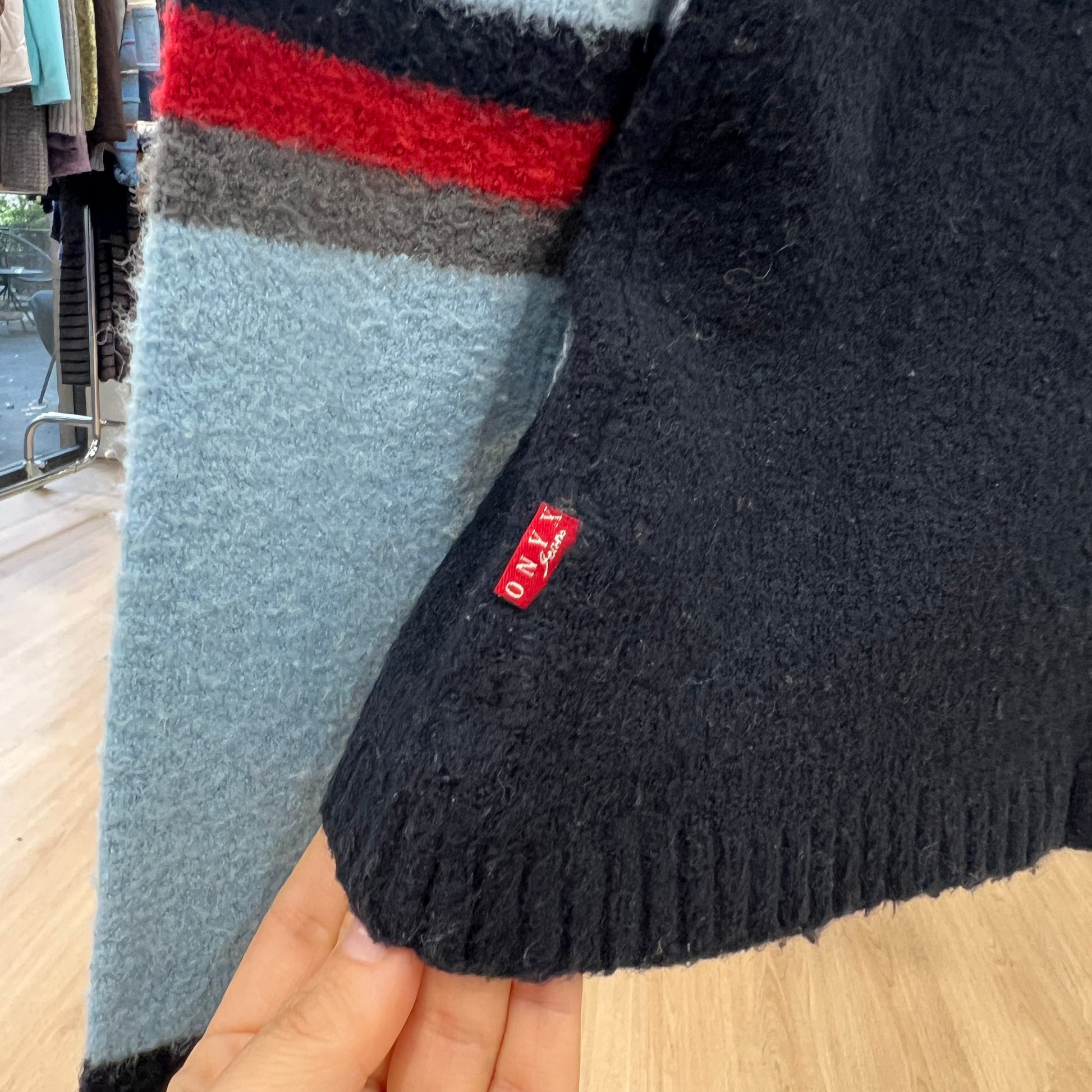 Close-up of a sweater with a brand label held by a hand on a wooden floor