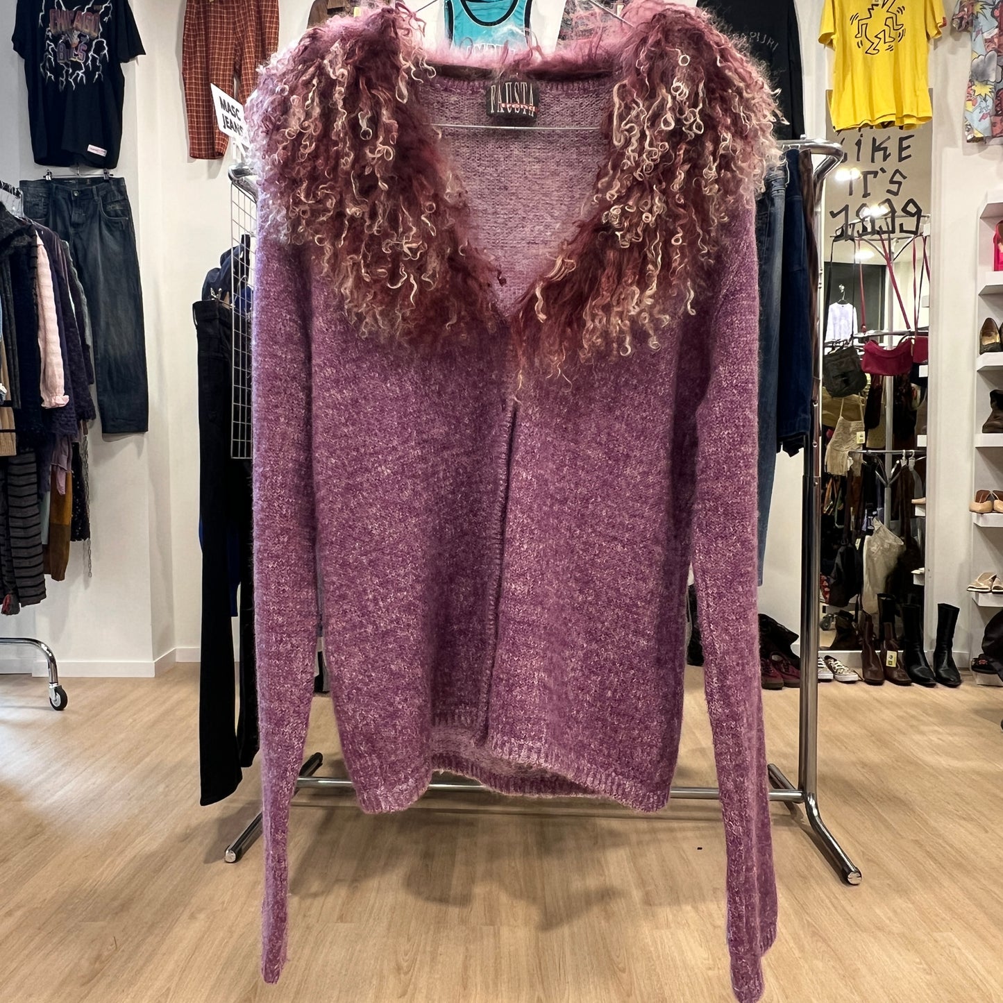 Purple sweater with curly sleeves on a rack in a store setting