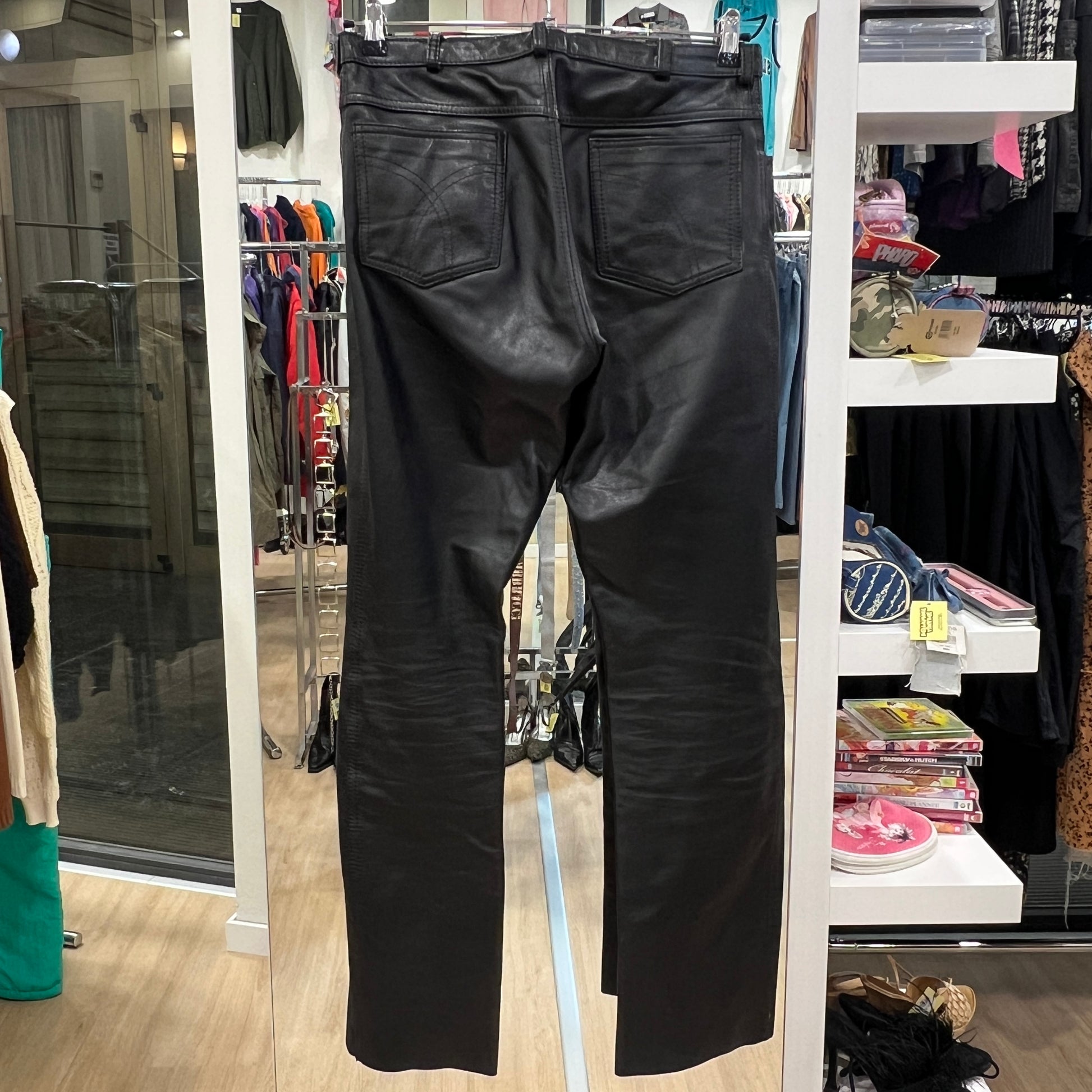 Black leather pants displayed in a store setting with clothing racks and shelves in the background