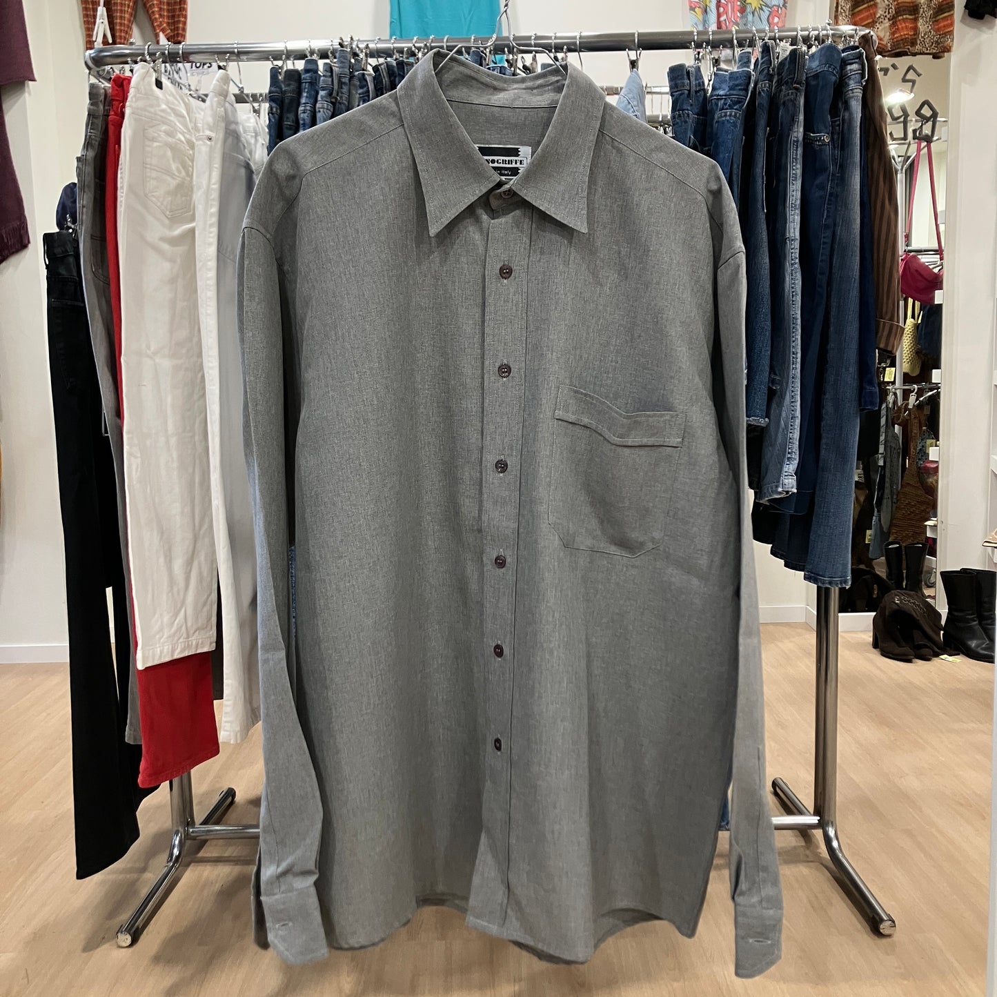 Gray button-up shirt on a rack with clothing in the background