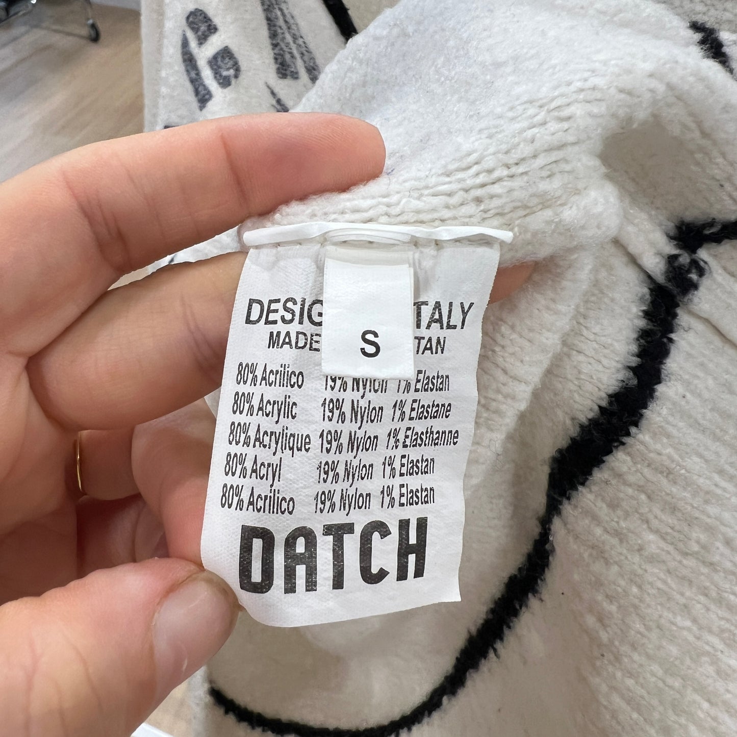 Hand holding a fabric label with 'DATCH' branding on a textured white and black fabric background
