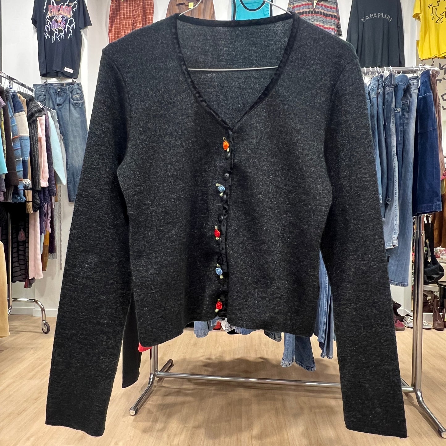 Dark gray cardigan with colorful buttons on a clothing rack in a store