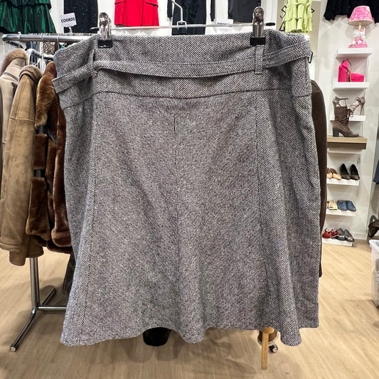 Gray herringbone skirt on a hanger in a store setting with clothing and shelves in the background
