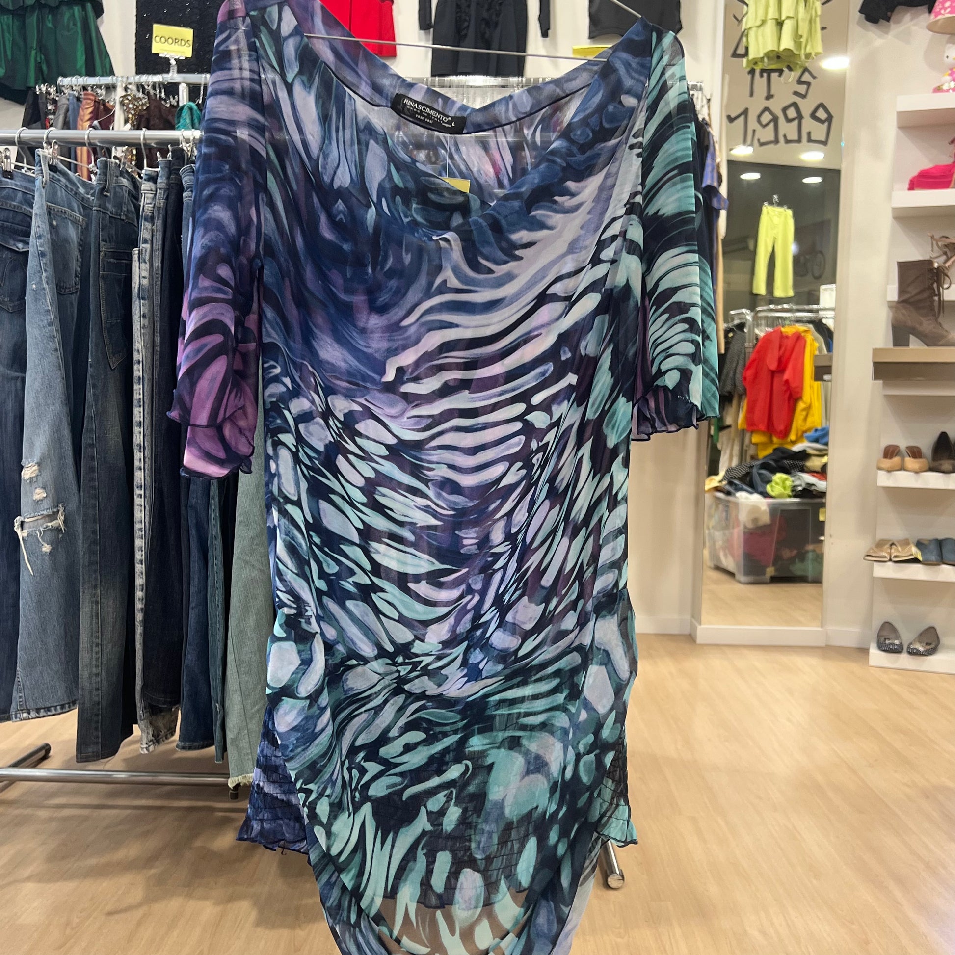 Blue and purple patterned dress hanging in a store with clothing racks and shelves in the background