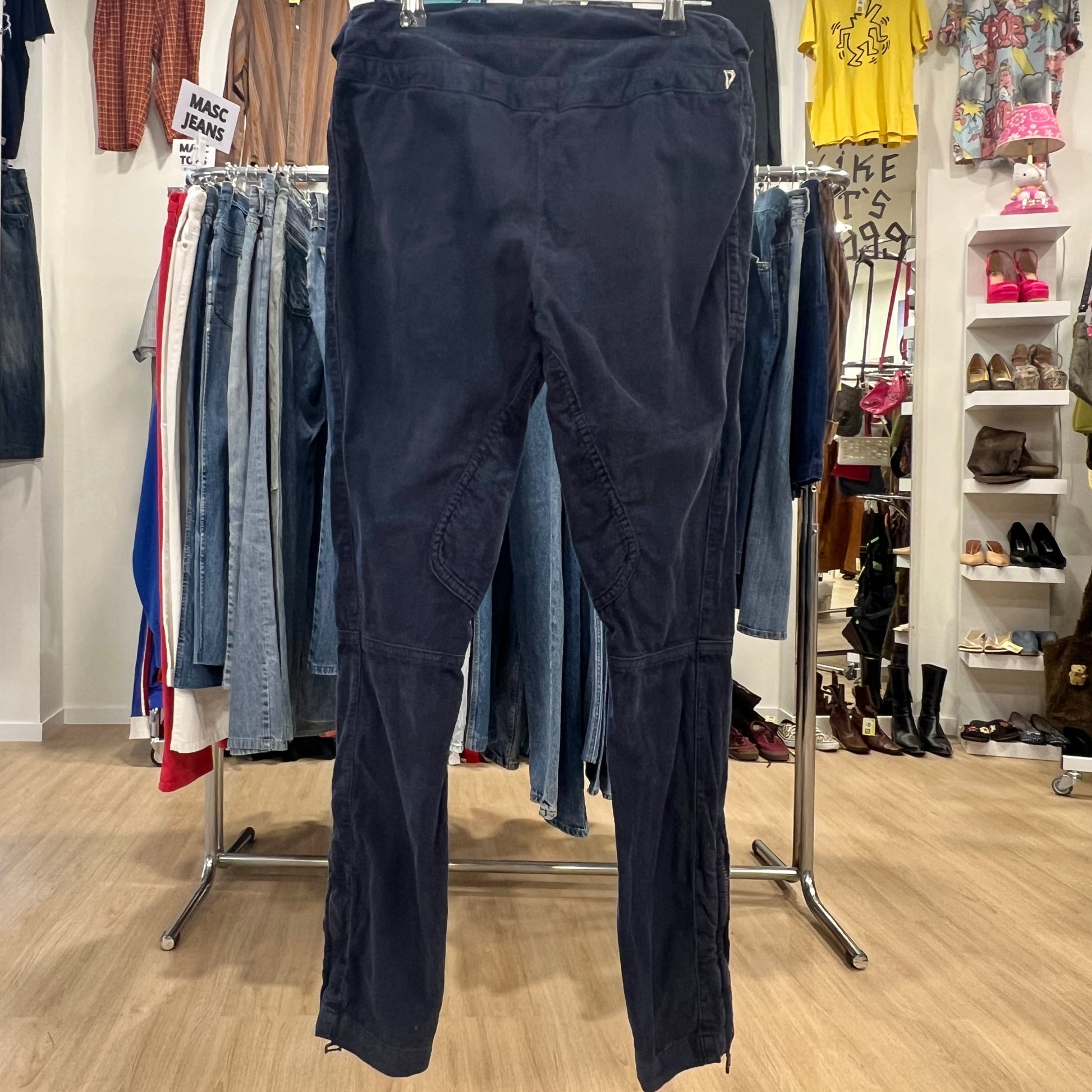 Navy blue pants hanging on a rack in a store with clothing and shoes in the background
