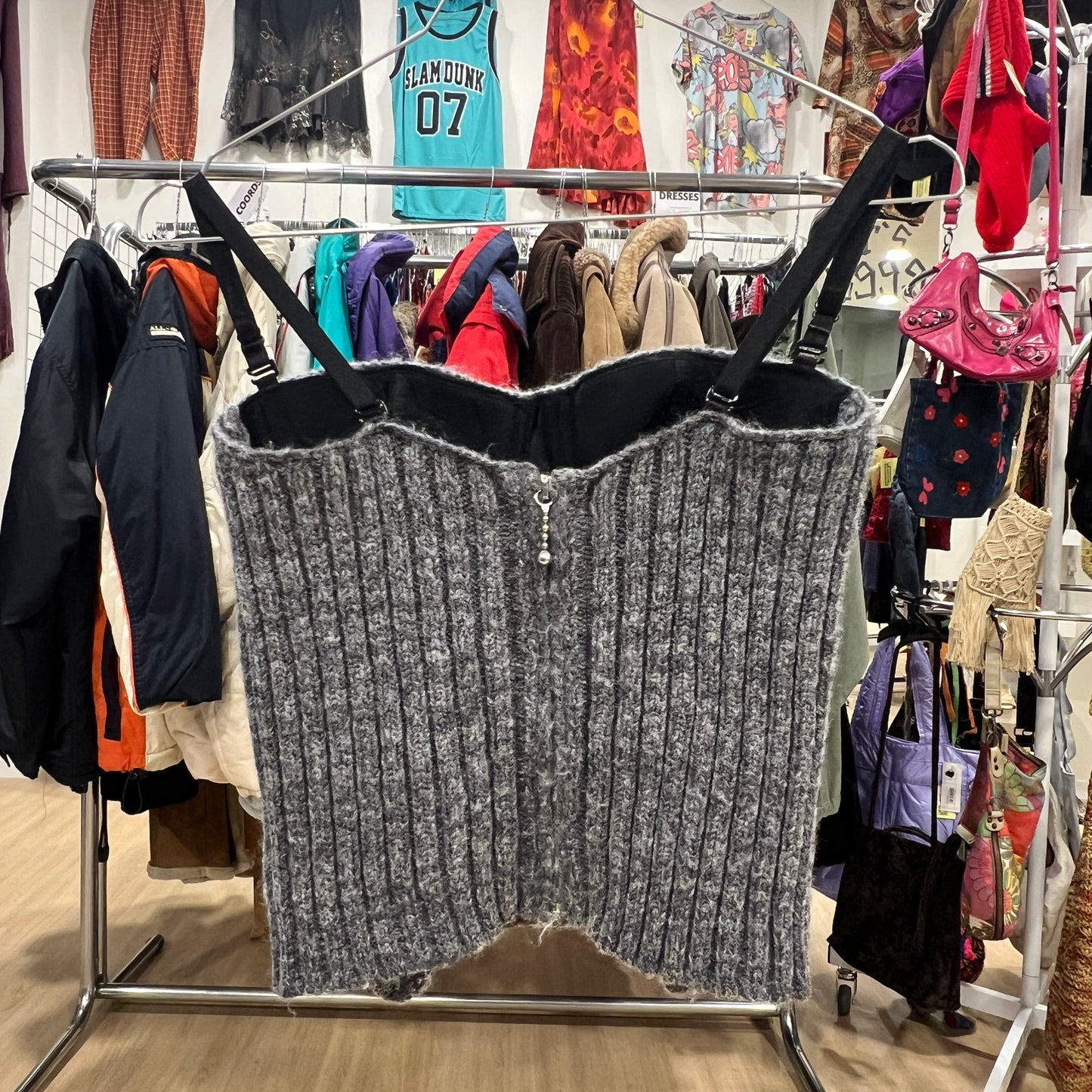 Gray ribbed knit sweater on a clothing rack with a background of various garments