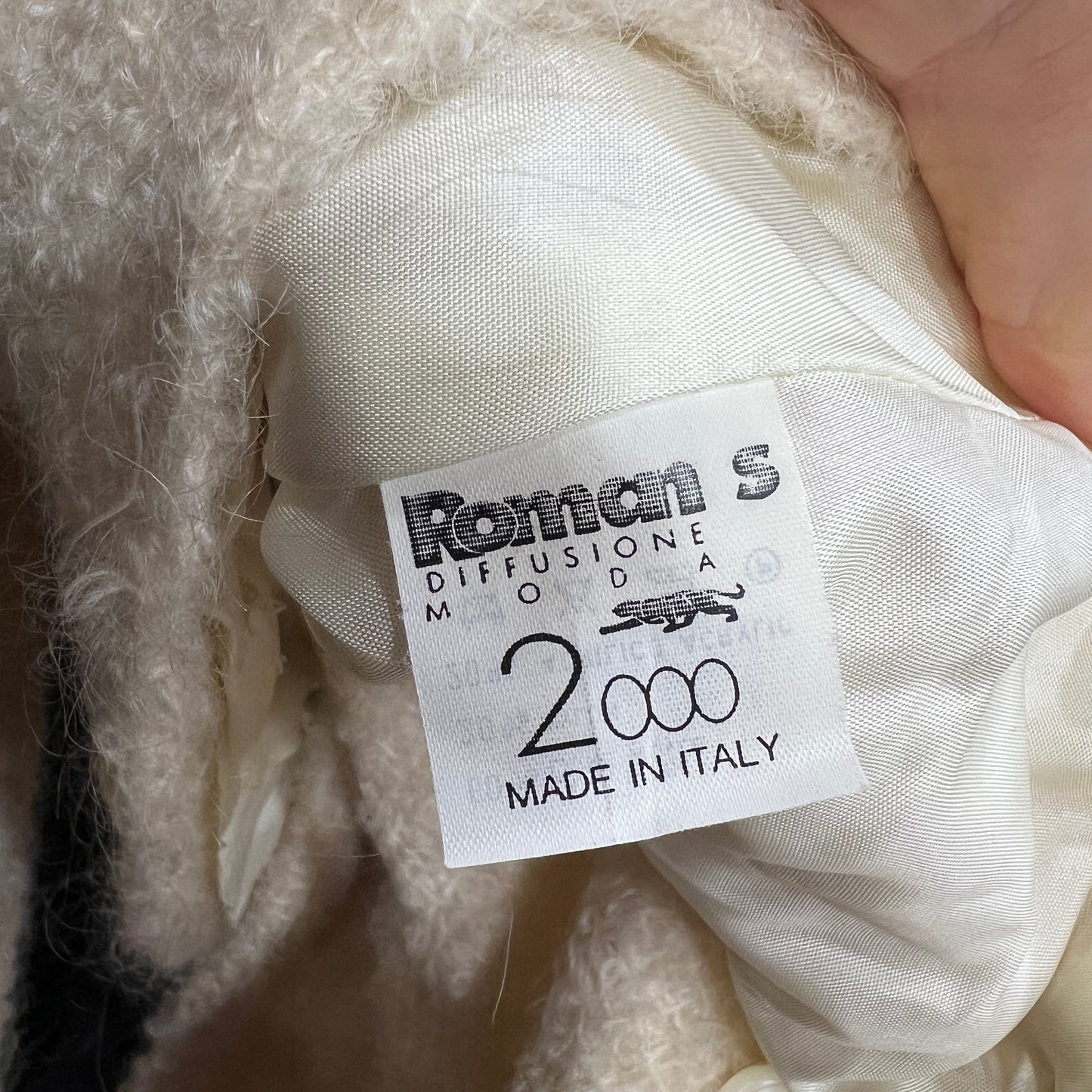 Label with 'Roman S Diffusione Moda 2000 Made in Italy' on a textured fabric background
