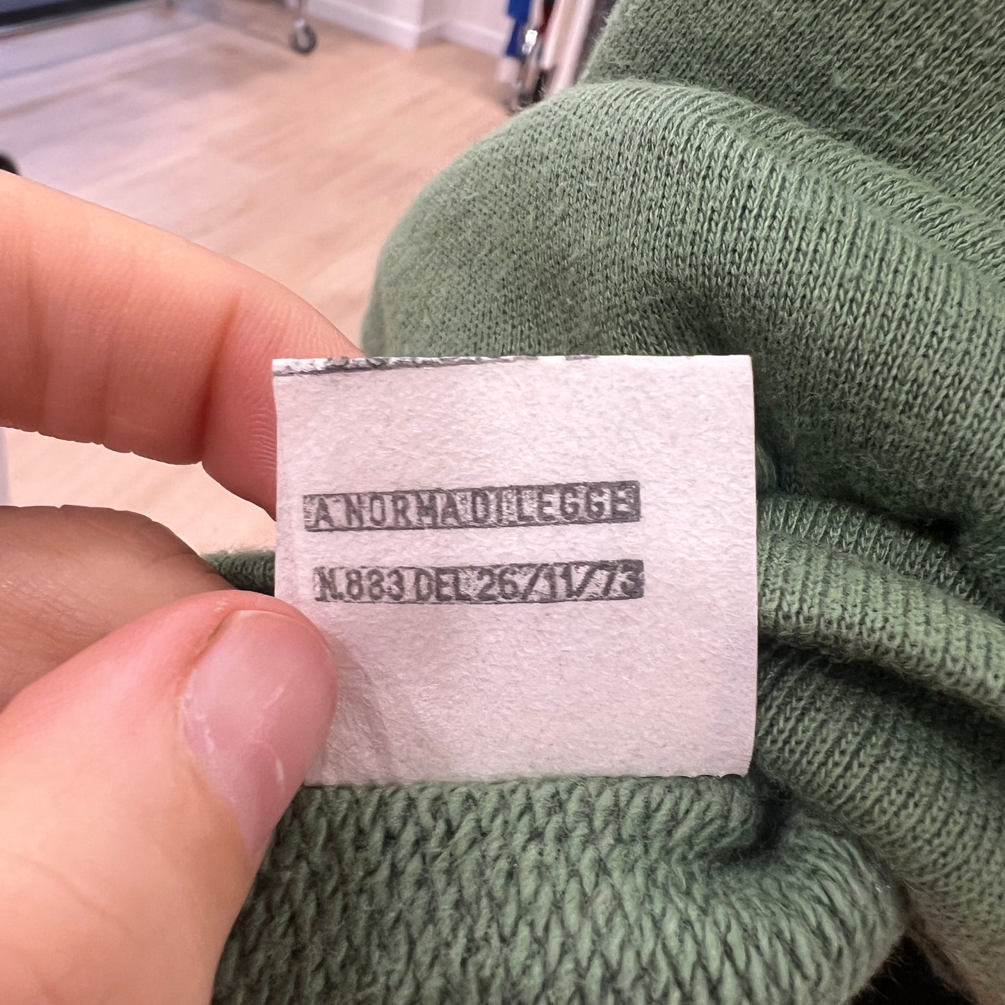 Close-up of a green sweater with a label held by a hand