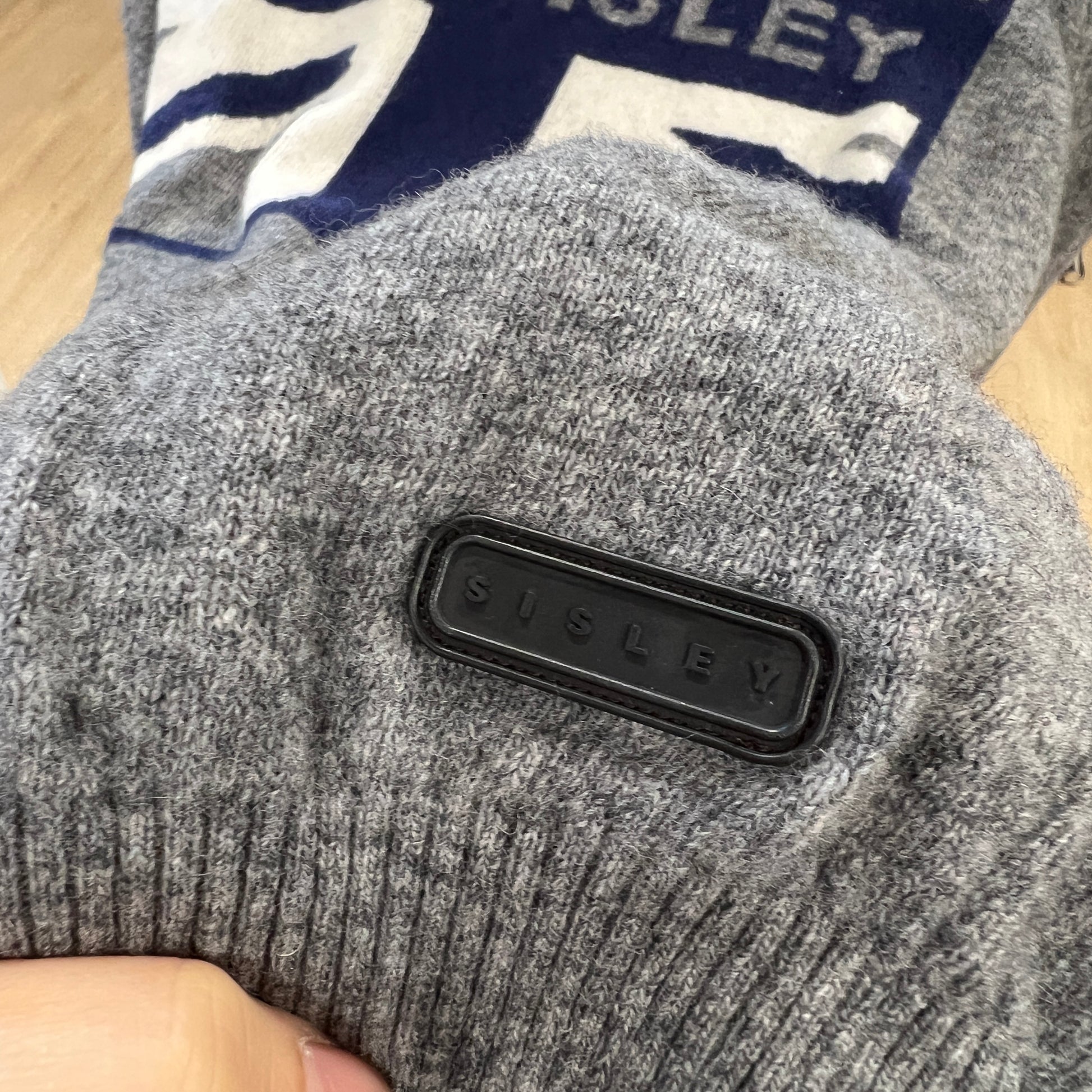 Gray knit sweater with a visible brand logo on a wooden surface