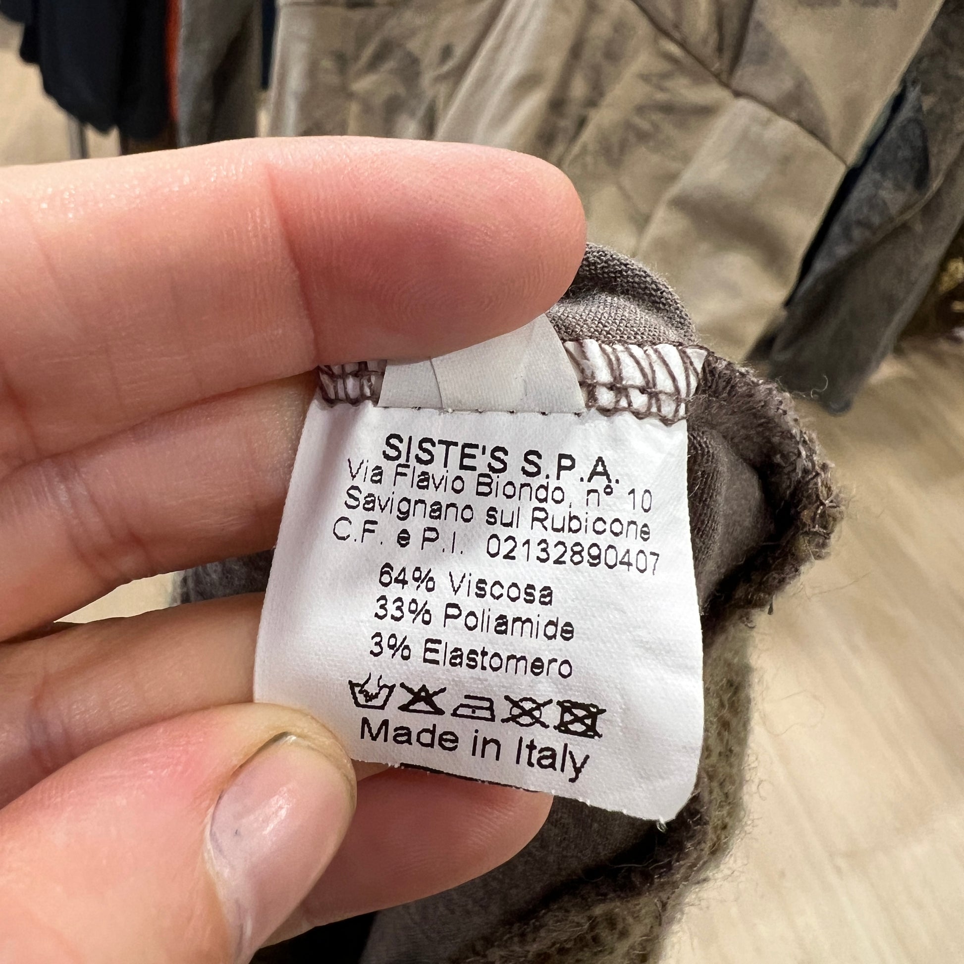 Clothing label held by a hand with text and product details