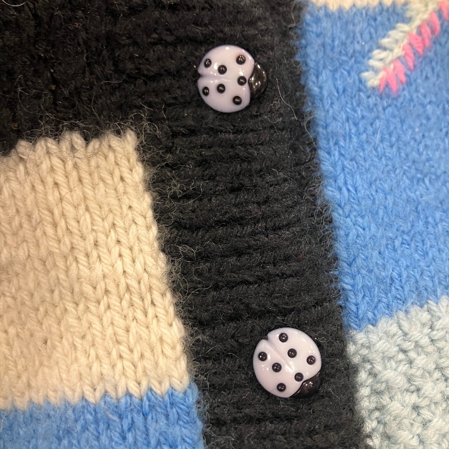 Close-up of a knitted fabric with two ladybug buttons on a multicolored background