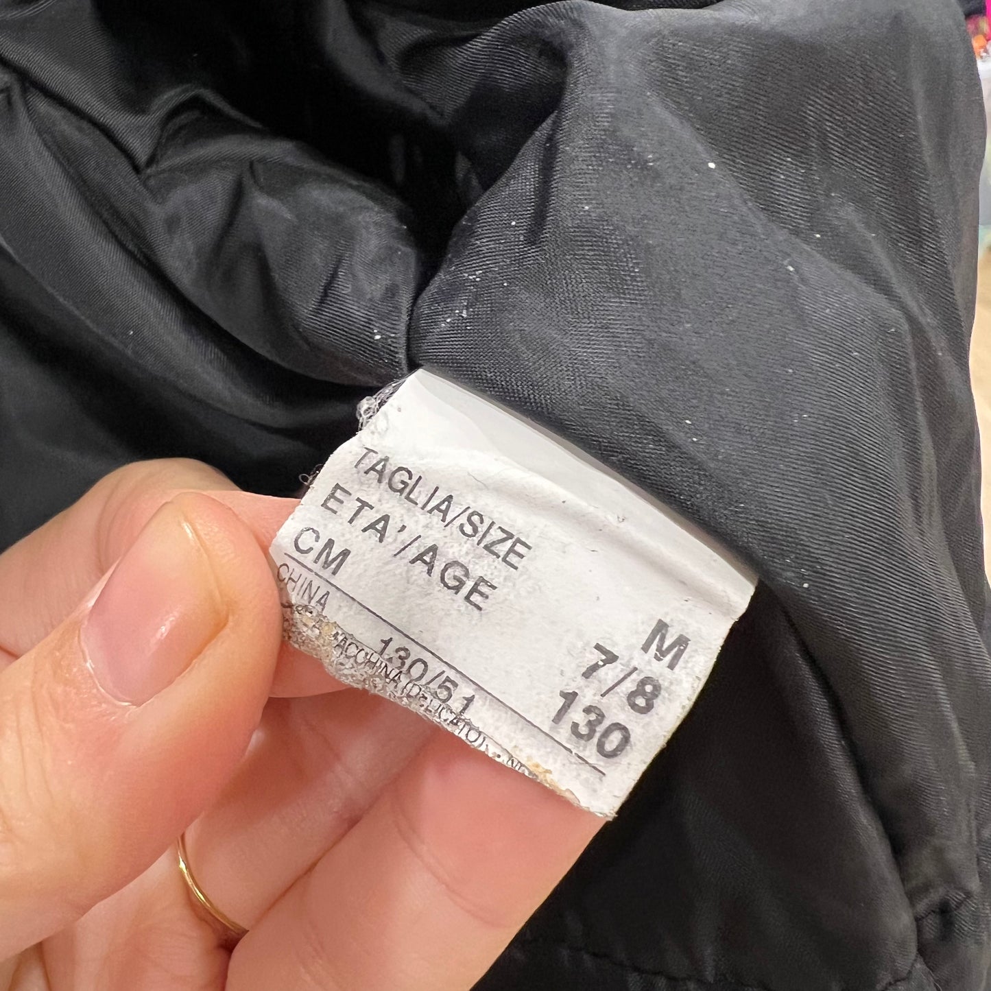 Hand holding a clothing tag with size information on a dark fabric background