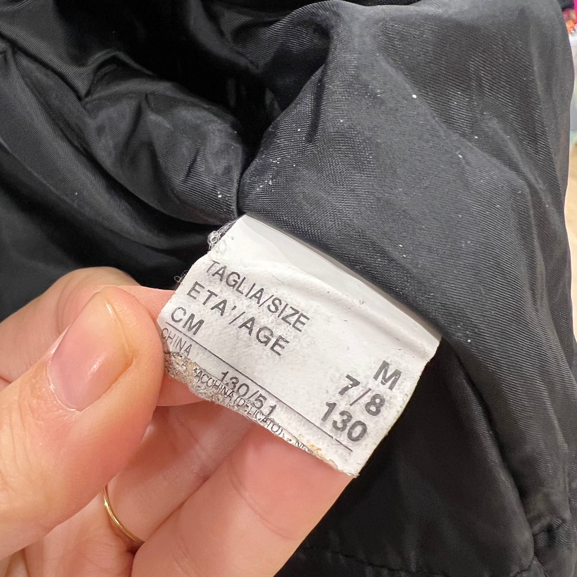 Hand holding a clothing tag with size information on a dark fabric background