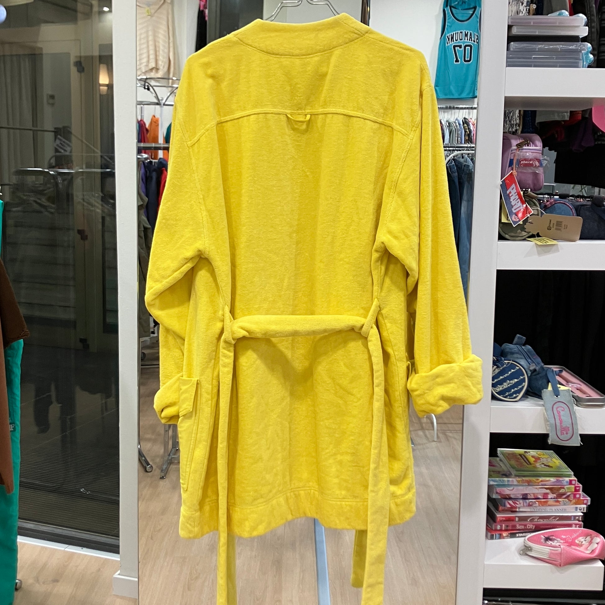 Back view of a bright yellow terry cloth bathrobe with a matching waist belt and rolled sleeves, displayed on

