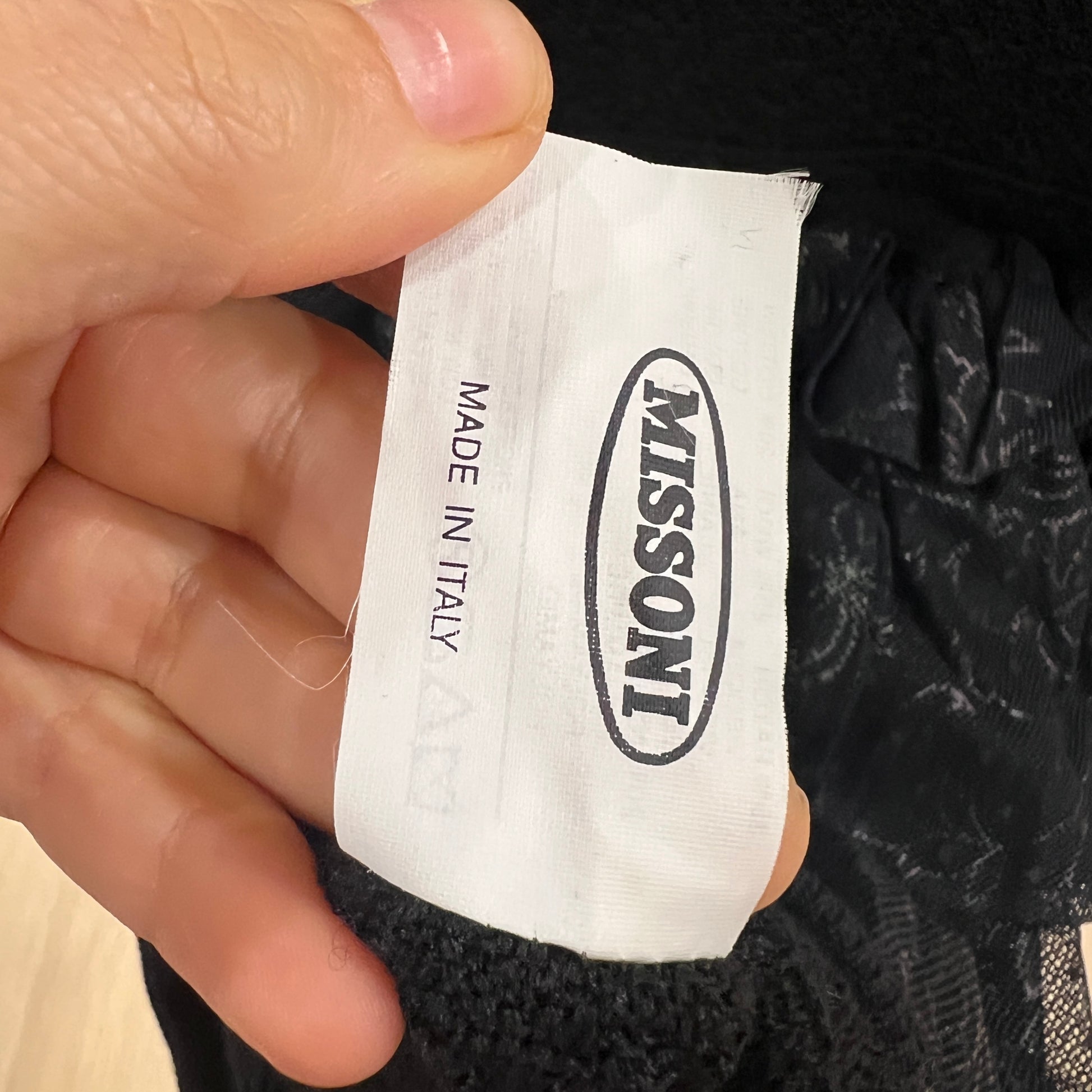 Hand holding a Missoni label with 'Made in Italy' text on a black garment