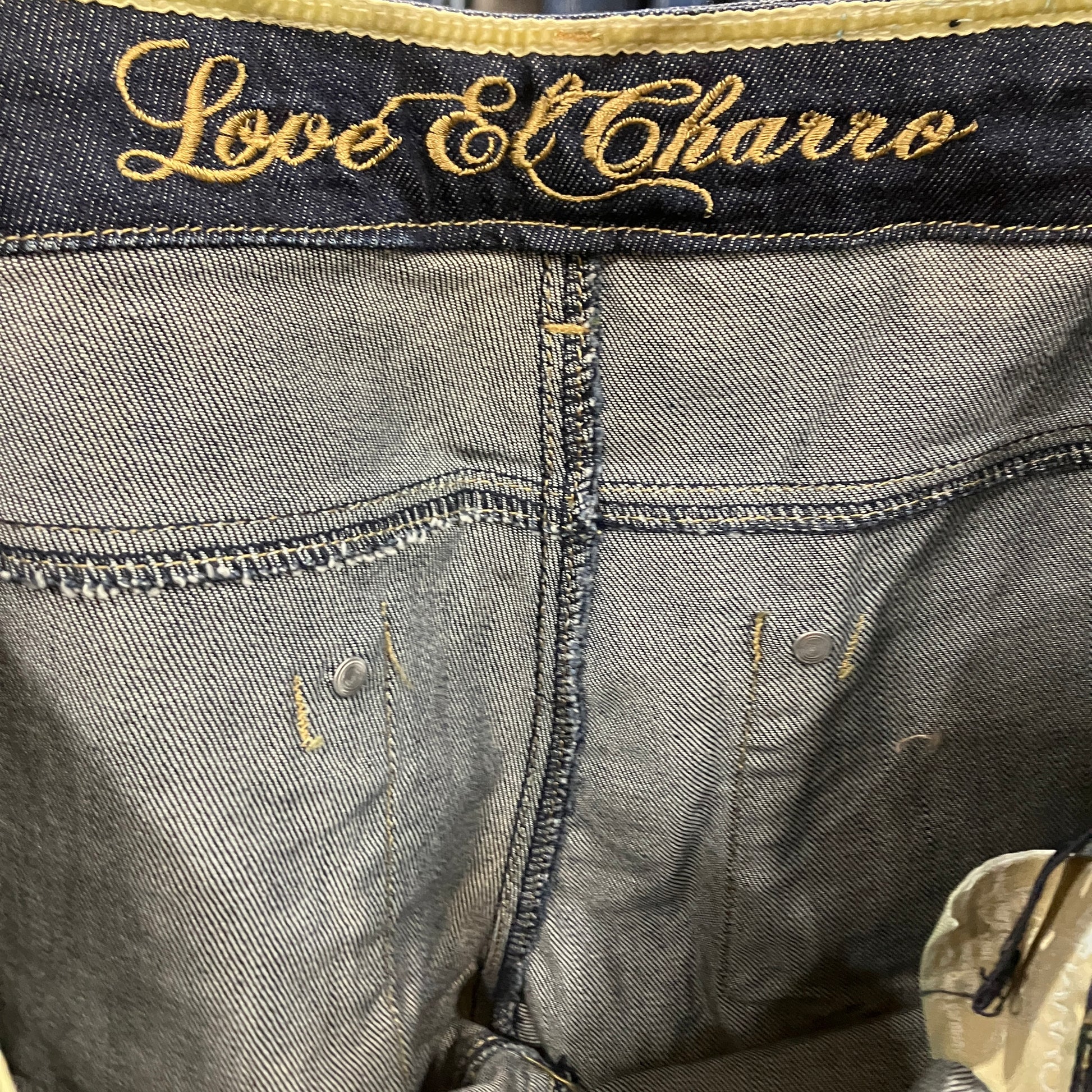Close-up of denim fabric with 'Love El Charro' embroidery on a dark background