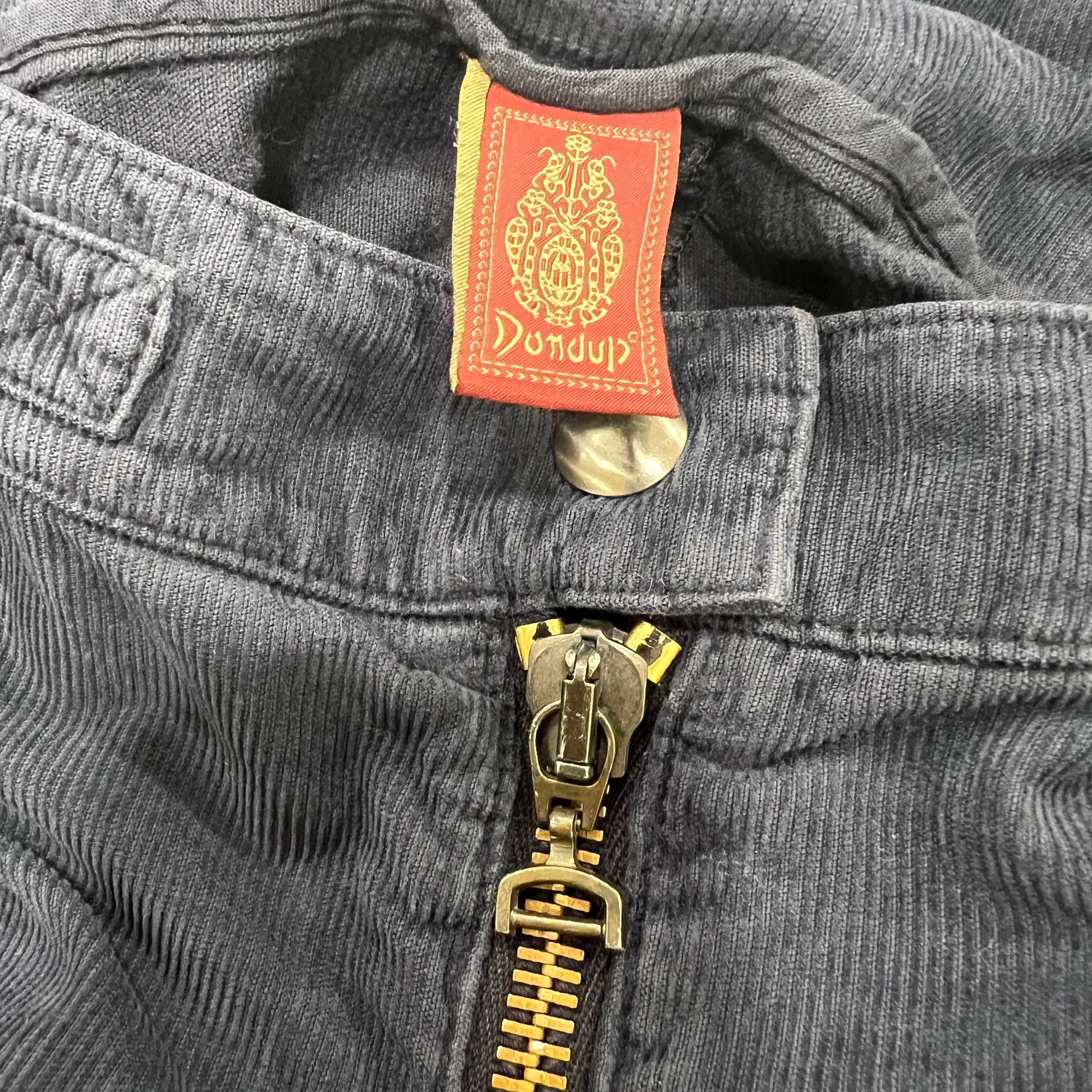 Close-up of a gray corduroy pants with a gold zipper and Dondup label