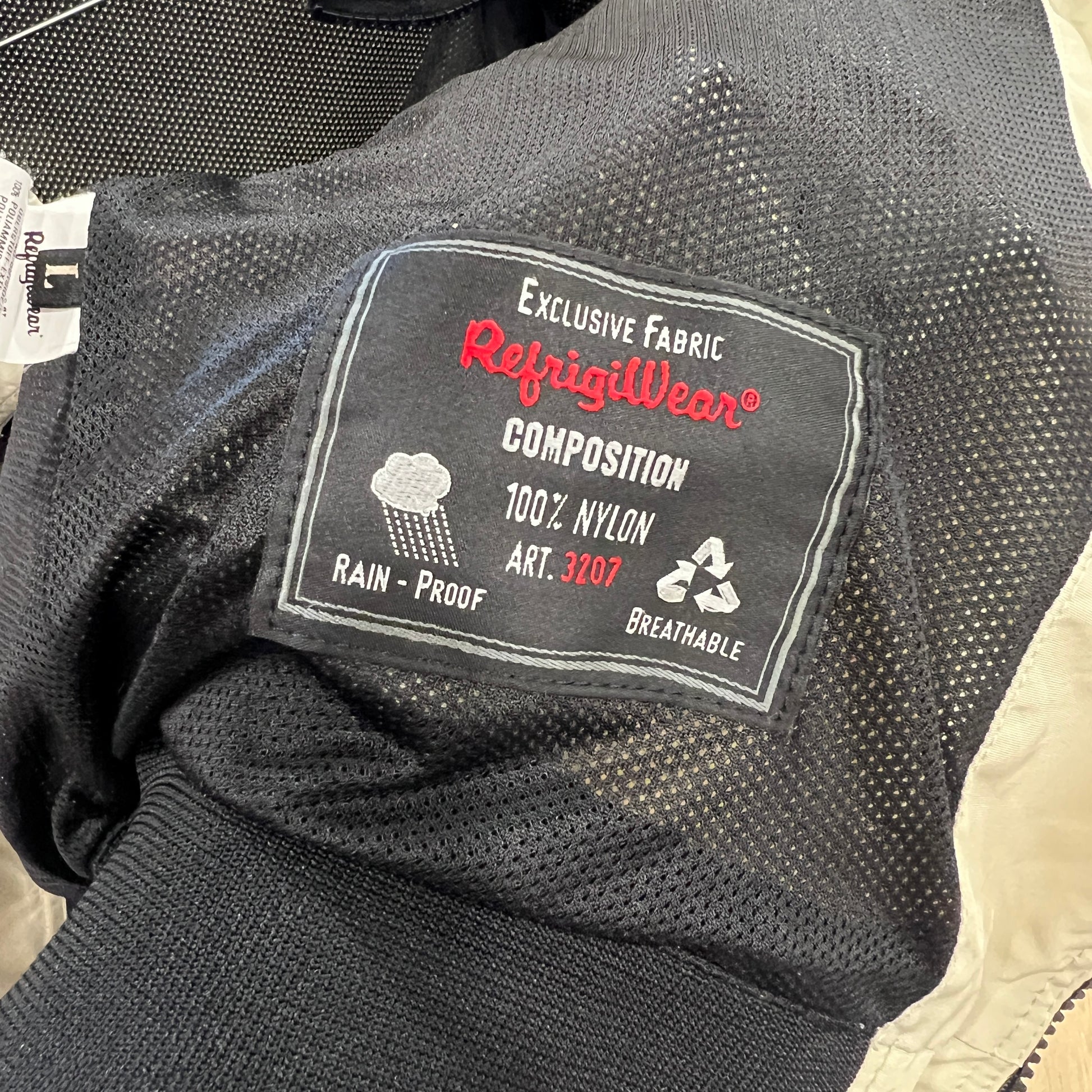 Close-up of a RefrigiWear inner label on a black mesh lining, showing composition 100% nylon, rain-proof and breathable features, and art. 3207

