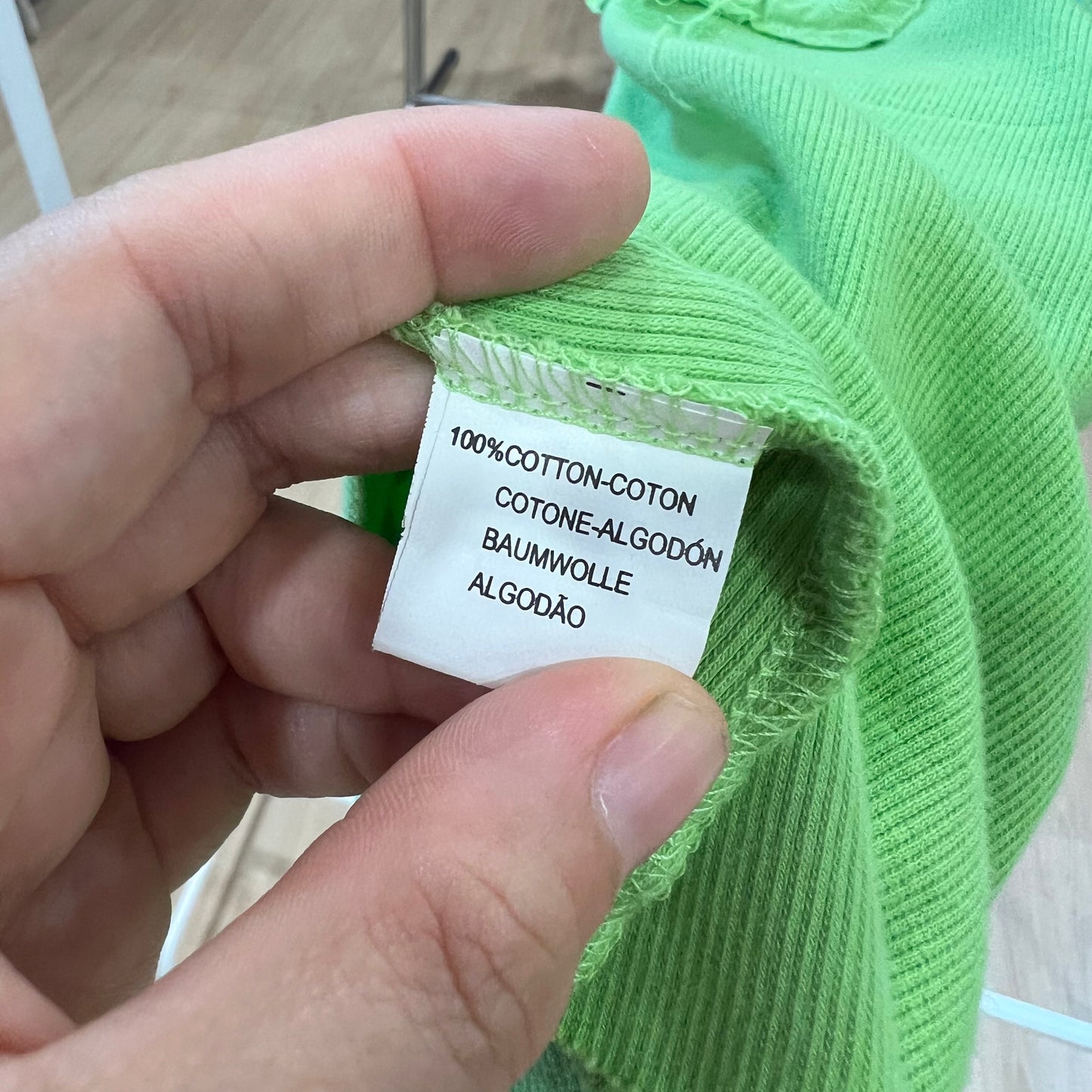 Hand holding a green garment with a label indicating 100% cotton.
