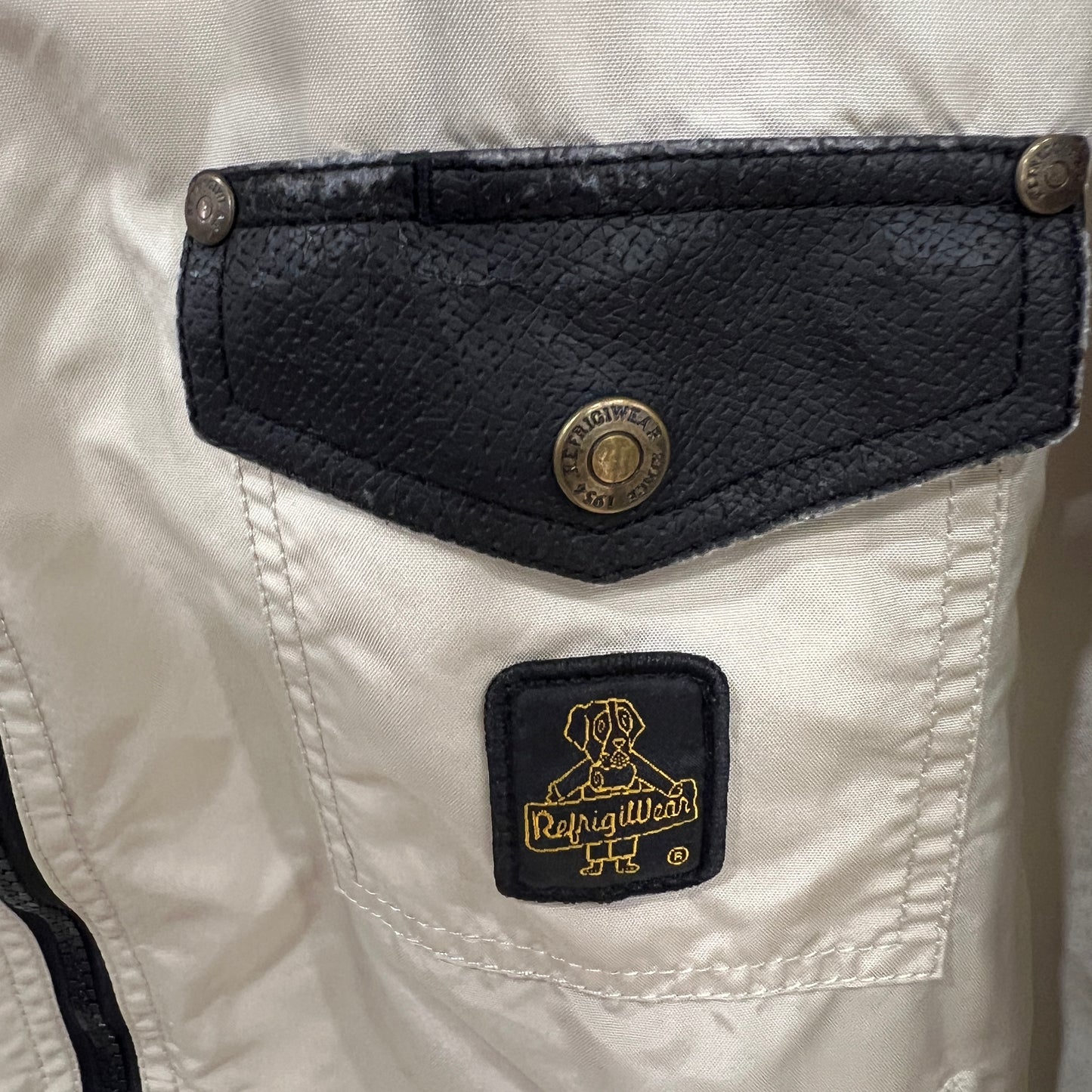 Close-up of a pocket on a white jacket with black leather trim and a brand logo